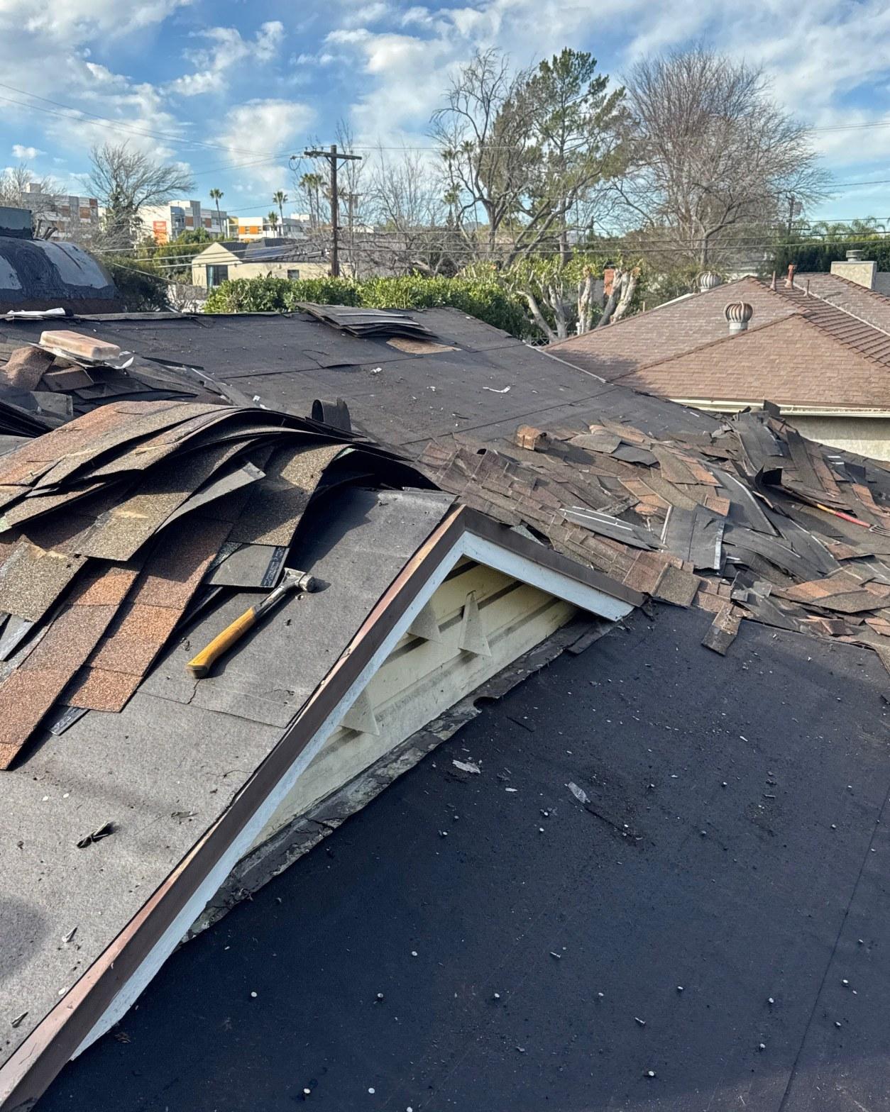 Two layers of old asphalt shingles stripped from residential roof exposing underlayment and decking, LA County reroof