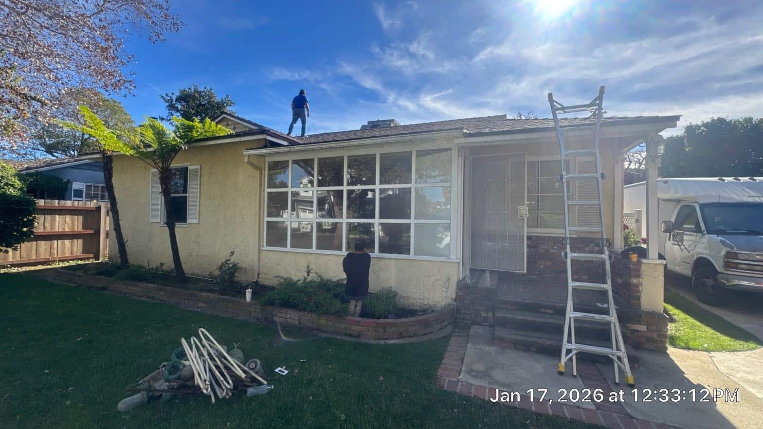 shingle-reroof-duration-cool-plus-los-angeles-3309 Roofer standing on low-slope asphalt shingle roof of single-story stucco house with white ladder propped against eave.