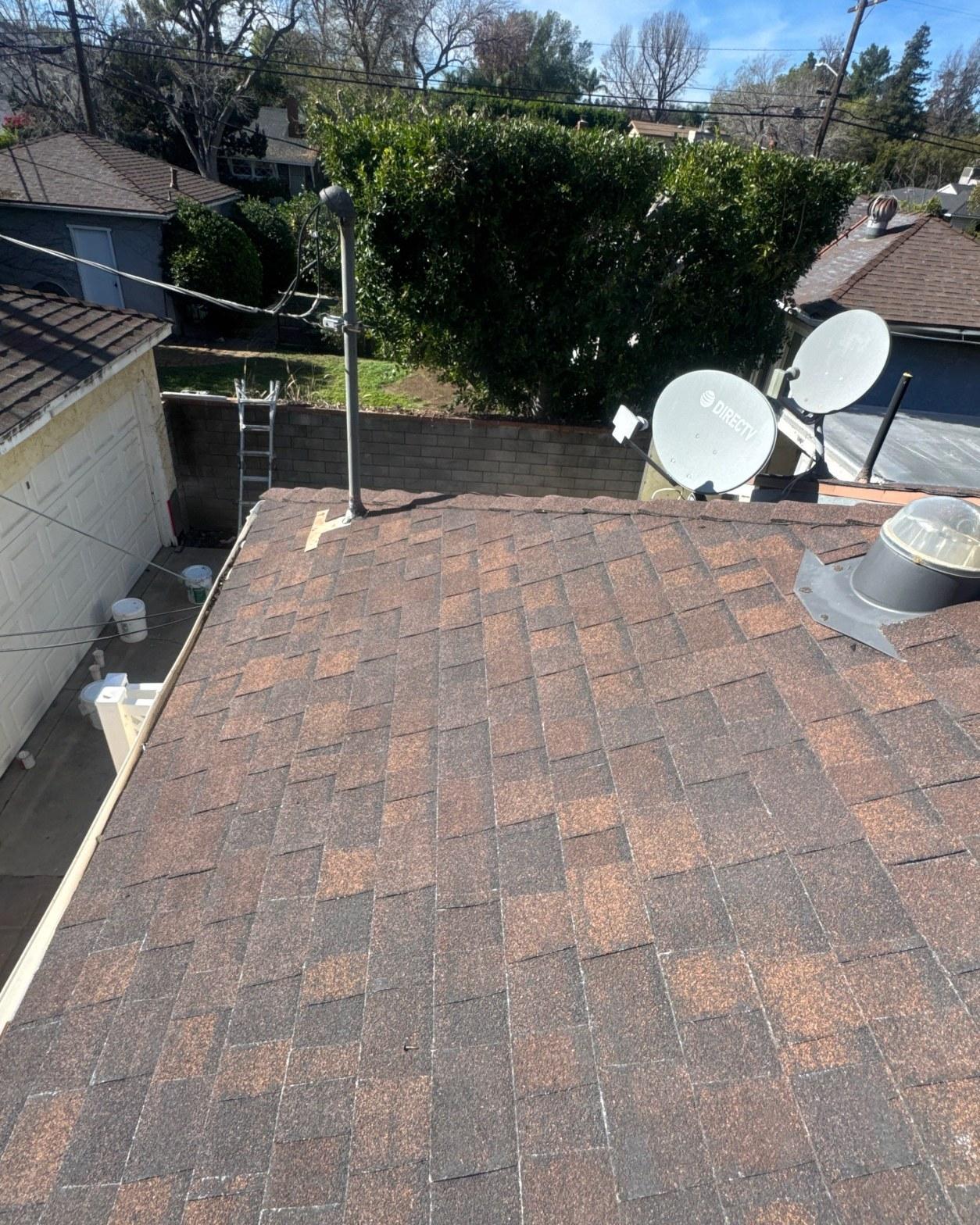 shingle-reroof-duration-cool-plus-los-angeles-3311 Freshly installed brown asphalt shingle roof with plumbing vent, skylight, and two DirecTV satellite dishes on residential home.