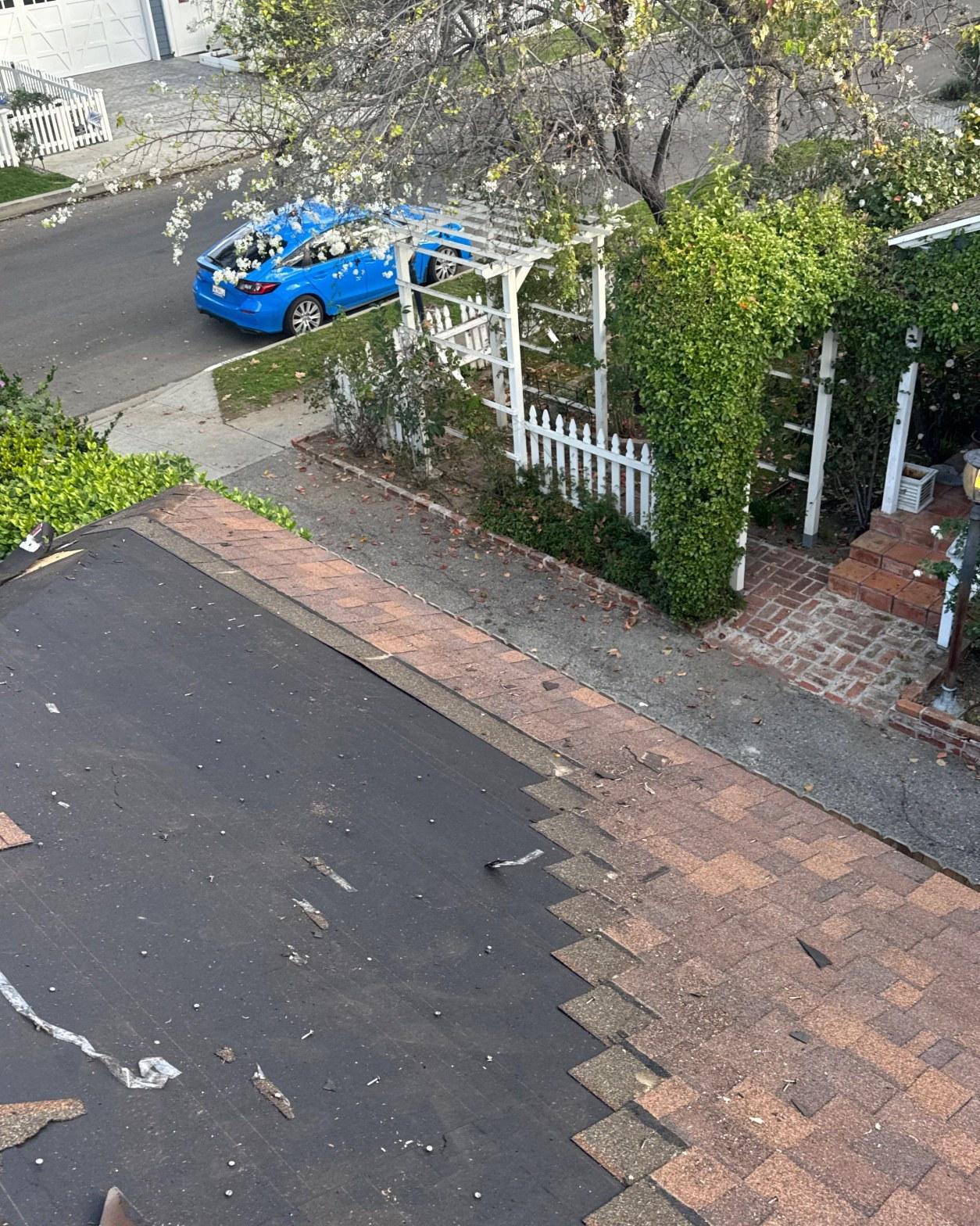 shingle-reroof-duration-cool-plus-los-angeles-3314 Residential roof tear-off in progress, black underlayment exposed beside remaining brown asphalt shingles, street view below.