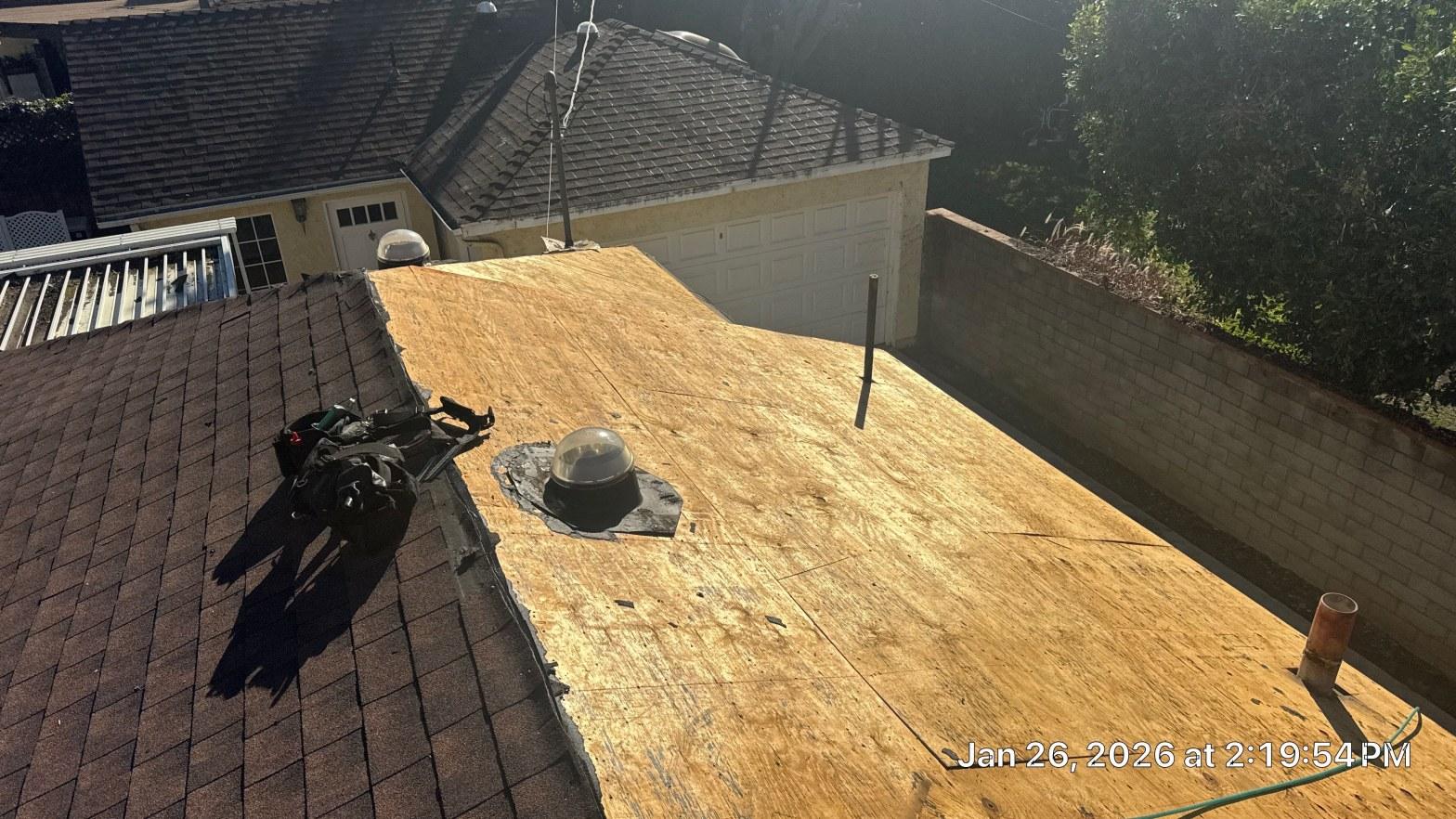 shingle-reroof-duration-cool-plus-los-angeles-3316 Residential flat roof tear-off showing bare OSB plywood decking, dome skylight, and pipe penetrations mid-replacement.