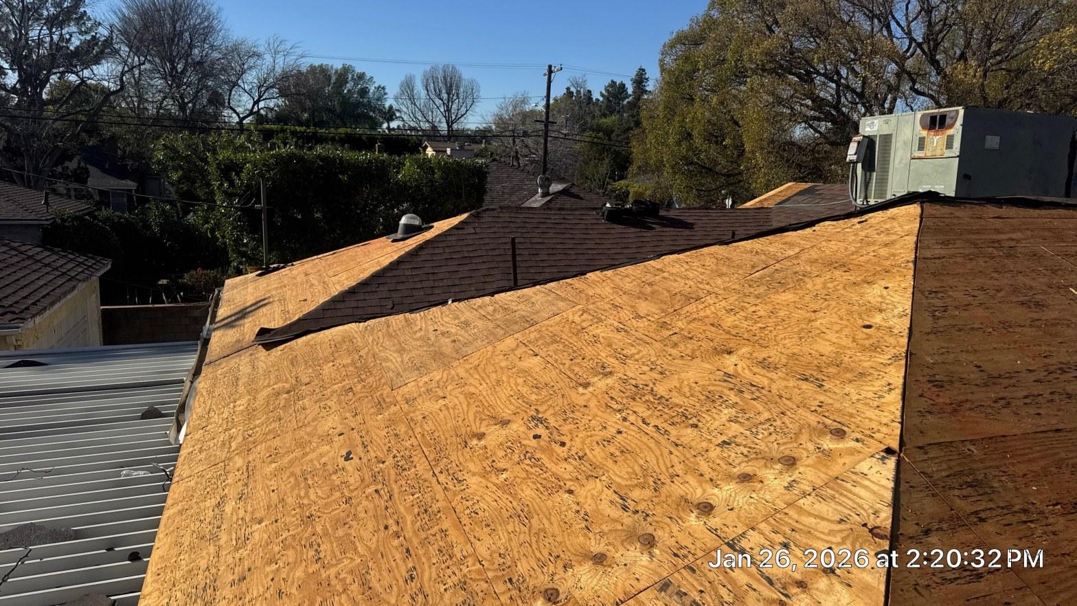 shingle-reroof-duration-cool-plus-los-angeles-3318 Bare plywood roof decking exposed after asphalt shingle tear-off on residential home, partial shingles remaining on ridge.