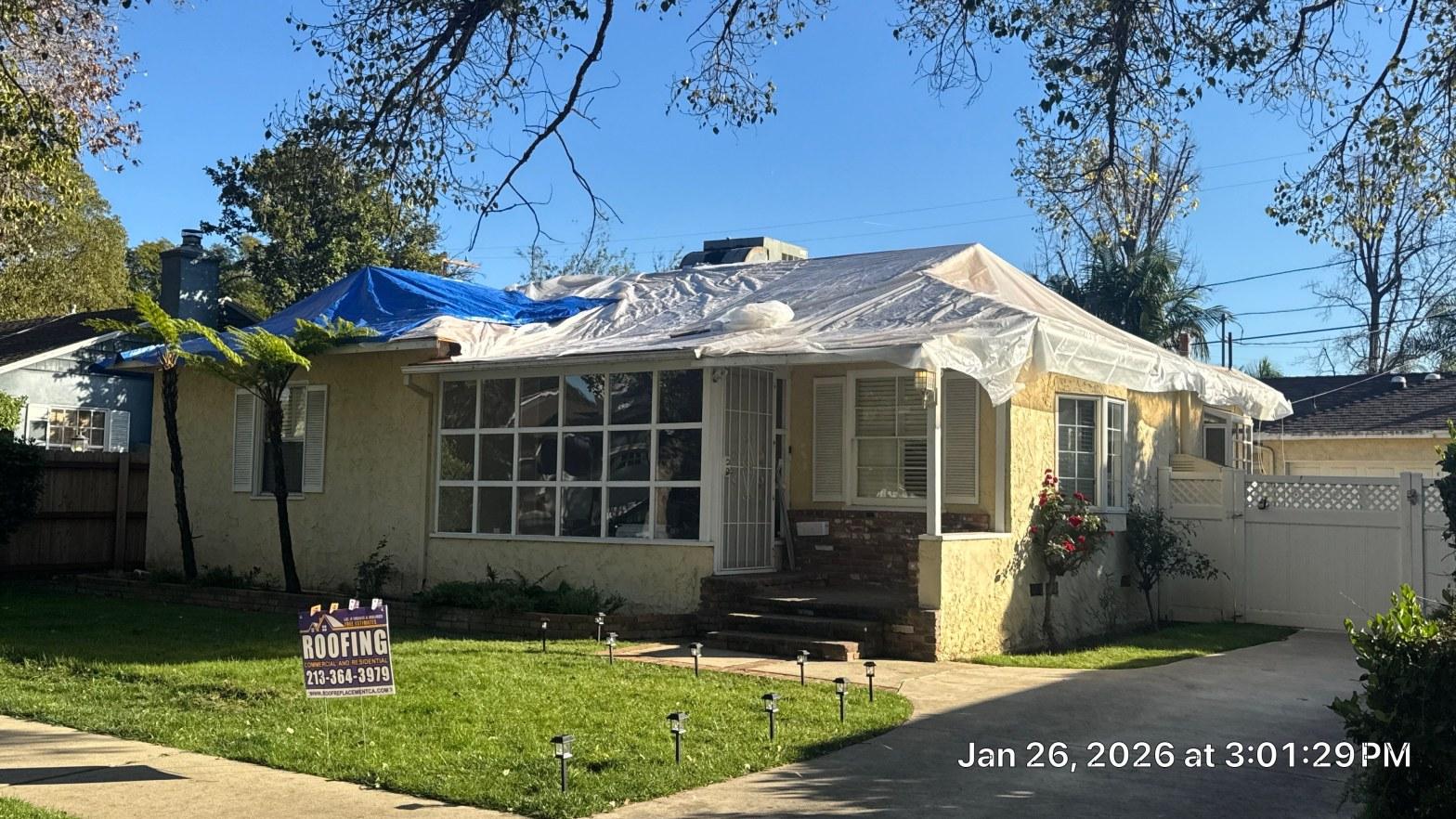 shingle-reroof-duration-cool-plus-los-angeles-3319 Single-story stucco home with white and blue tarps over roof during replacement, roofing company sign in front yard.