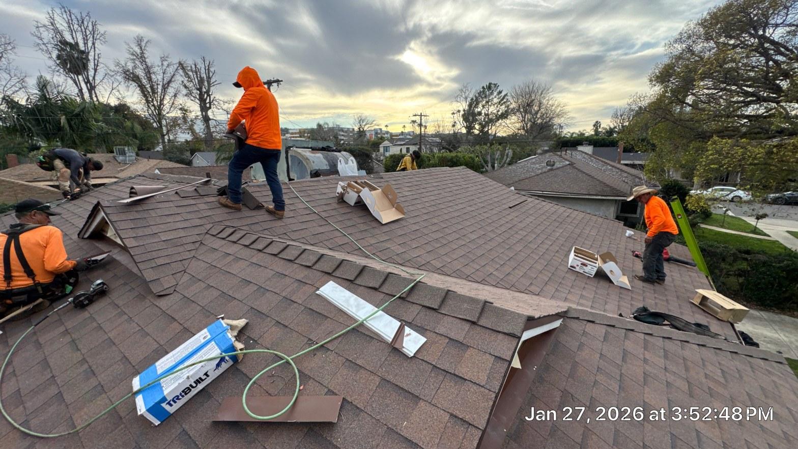 shingle-reroof-duration-cool-plus-los-angeles-3320 Roofing crew in orange shirts laying brown asphalt shingles on multi-slope residential roof with TribuIlt materials visible.