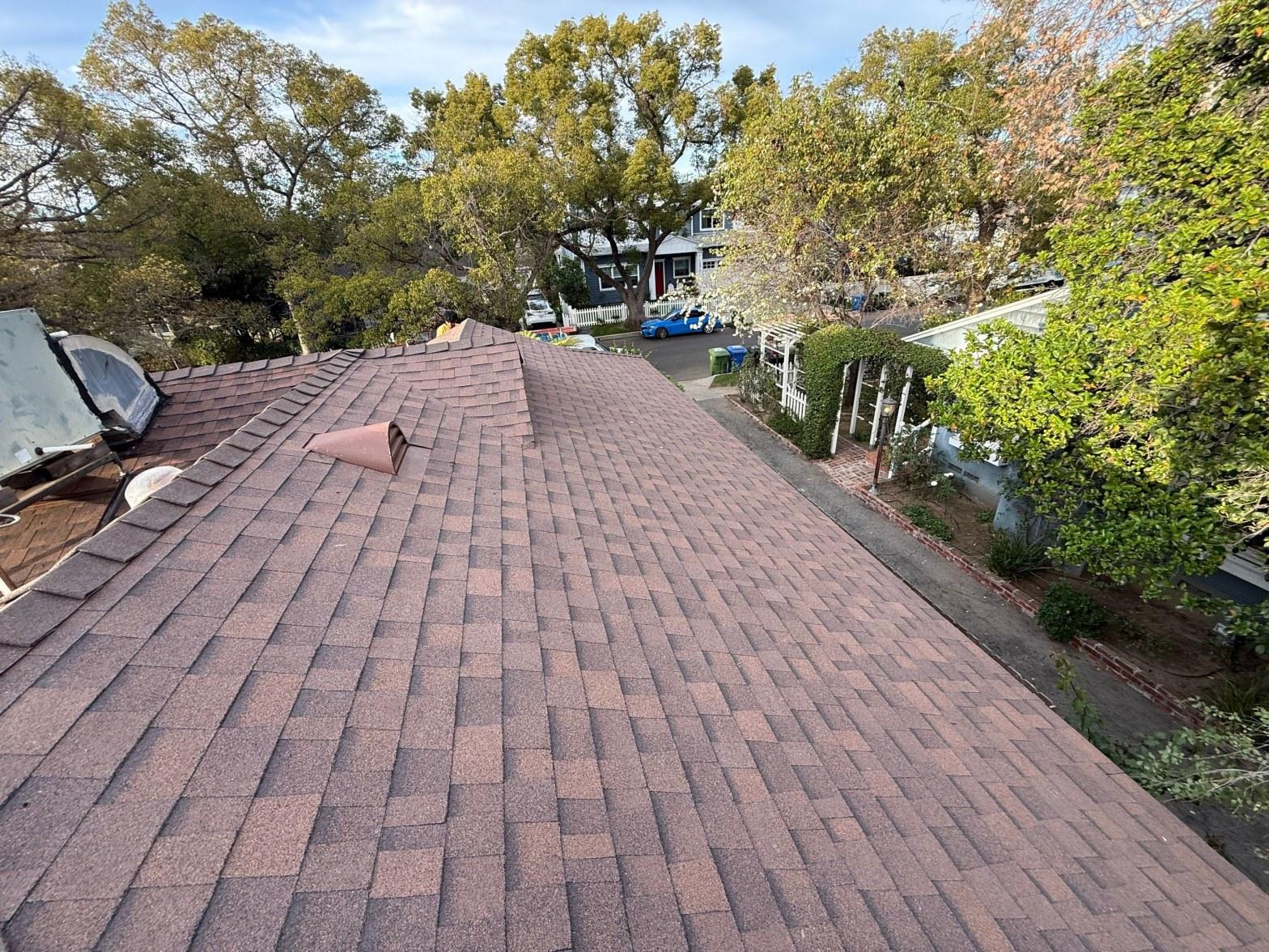 shingle-reroof-duration-cool-plus-los-angeles-3321 Aerial view of completed brown asphalt shingle roof with pipe vent, surrounded by trees in residential neighborhood.