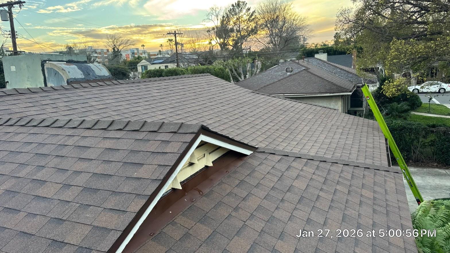shingle-reroof-duration-cool-plus-los-angeles-3322 Freshly installed brown asphalt shingle roof with dormer detail and green ladder visible at sunset.