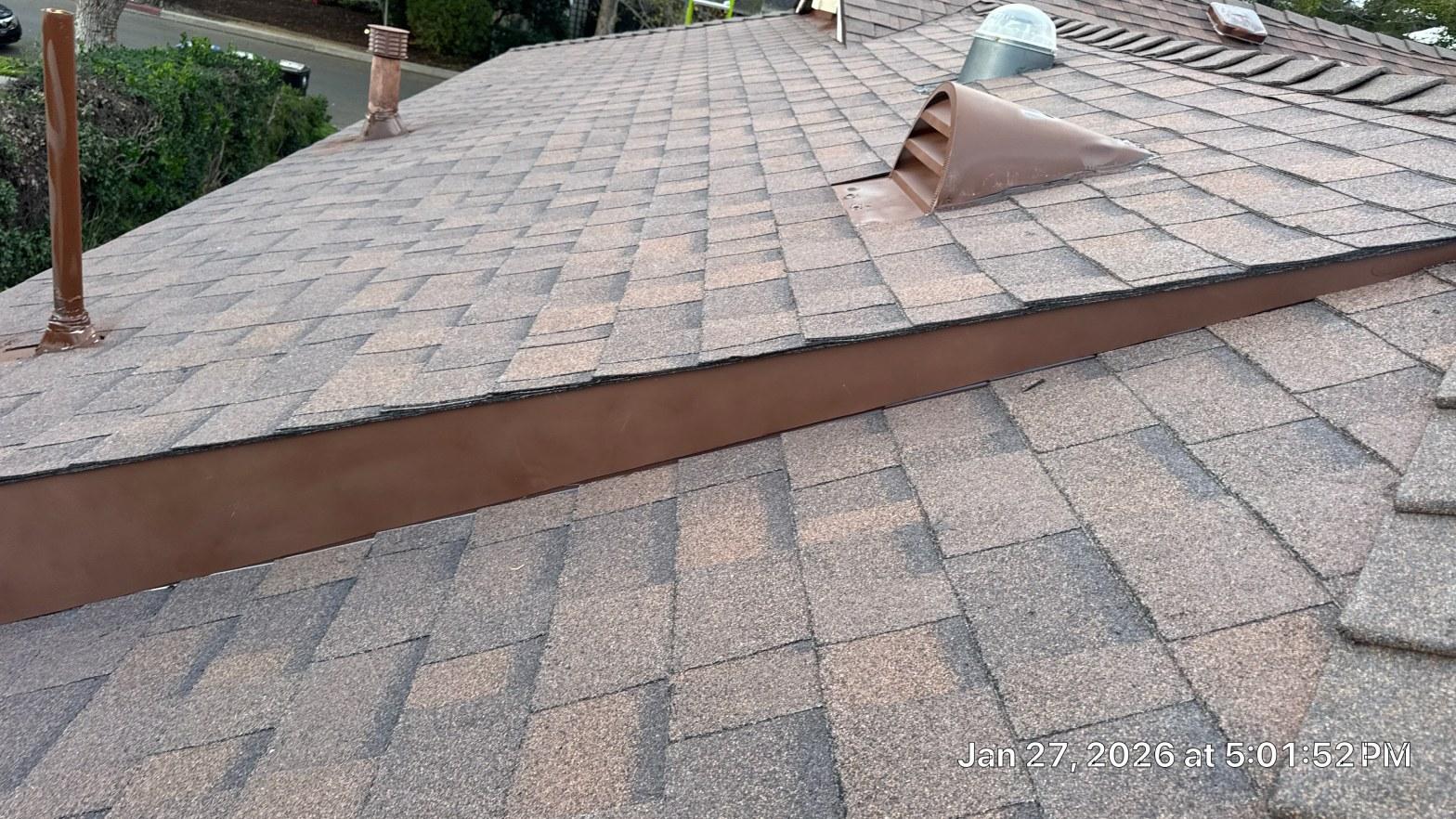 shingle-reroof-duration-cool-plus-los-angeles-3325 Brown metal step flashing at roof level change on asphalt shingle roof with exhaust vents visible.