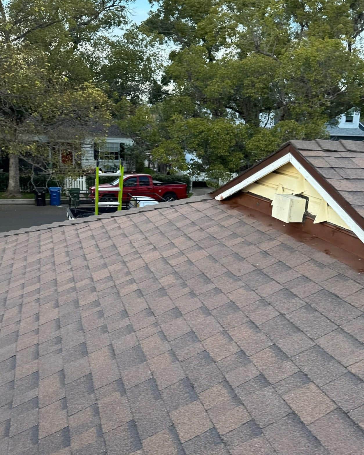 shingle-reroof-duration-cool-plus-los-angeles-3326 Brown asphalt shingle roof with open dormer vent showing exposed yellow fascia board during roofing repair.