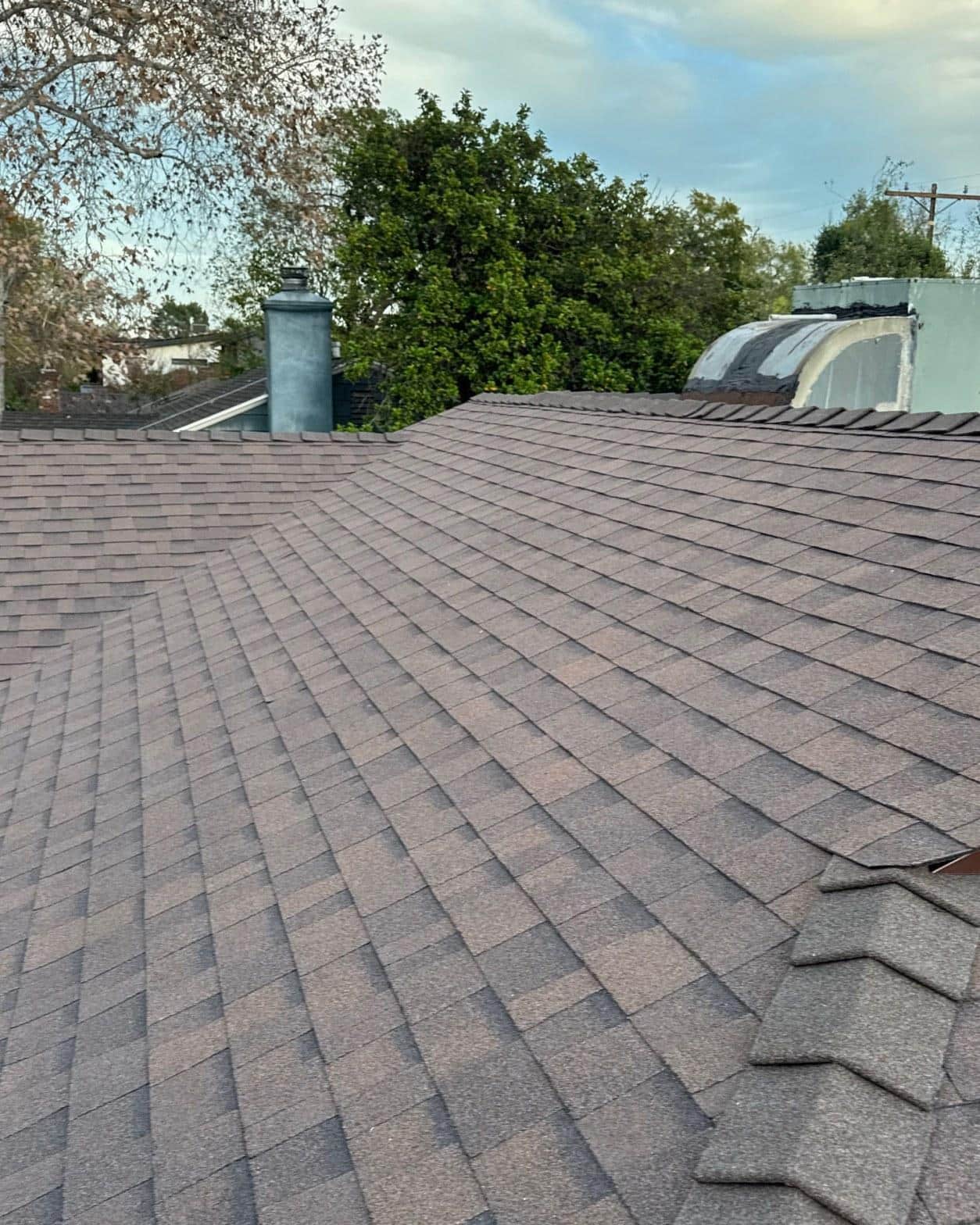 shingle-reroof-duration-cool-plus-los-angeles-3327 Freshly installed brown asphalt shingle roof with metal chimney flue and hip ridge on residential home.