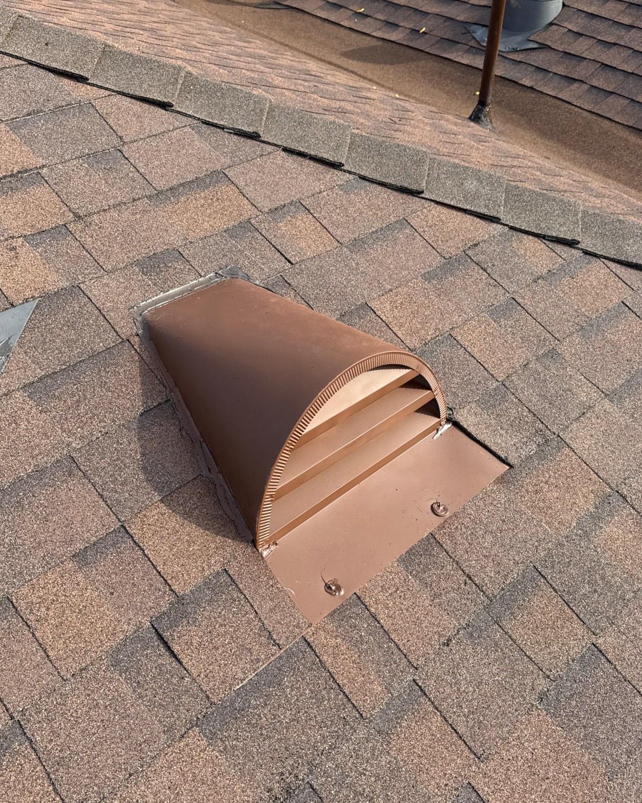 shingle-reroof-duration-cool-plus-los-angeles-3330 Brown metal roof exhaust vent cap mounted on brown asphalt shingles with louvered opening facing downslope.