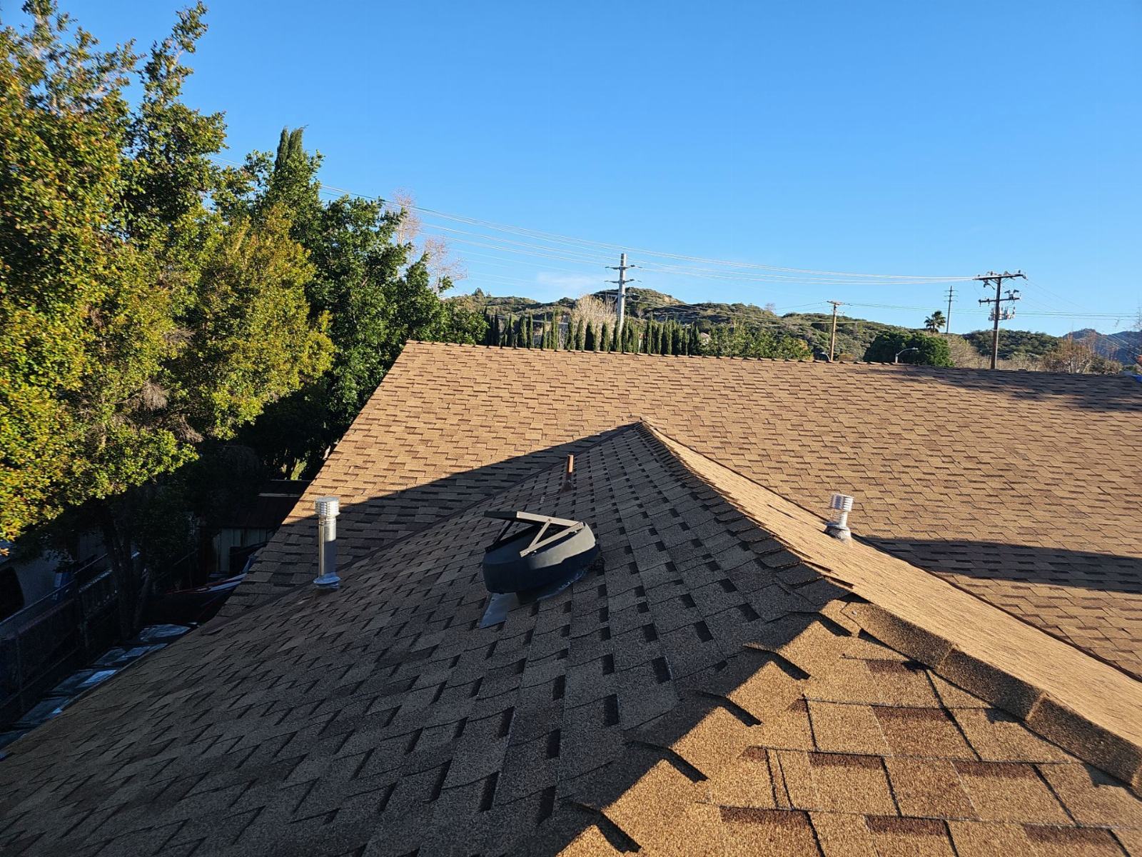 Partial reroof showing new dark shingles beside existing tan shingles, vents visible | Roof Replacement Inc Partial reroof showing new dark shingles beside existing tan shingles, vents visible — Roof Replacement Inc
