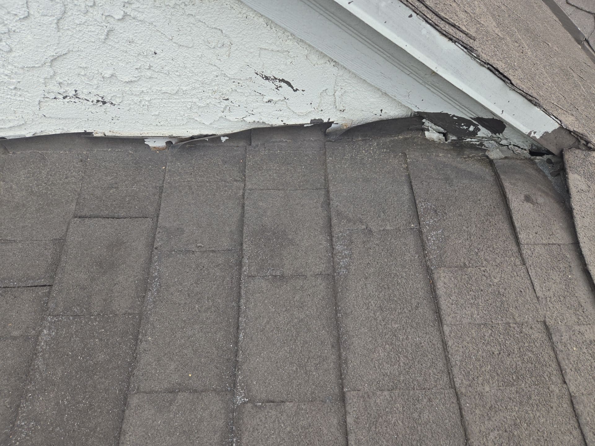 Damaged shingle roof edge meeting deteriorated stucco wall flashing in North Hollywood | Roof Replacement Inc Damaged shingle roof edge meeting deteriorated stucco wall flashing — North Hollywood — Roof Replacement Inc