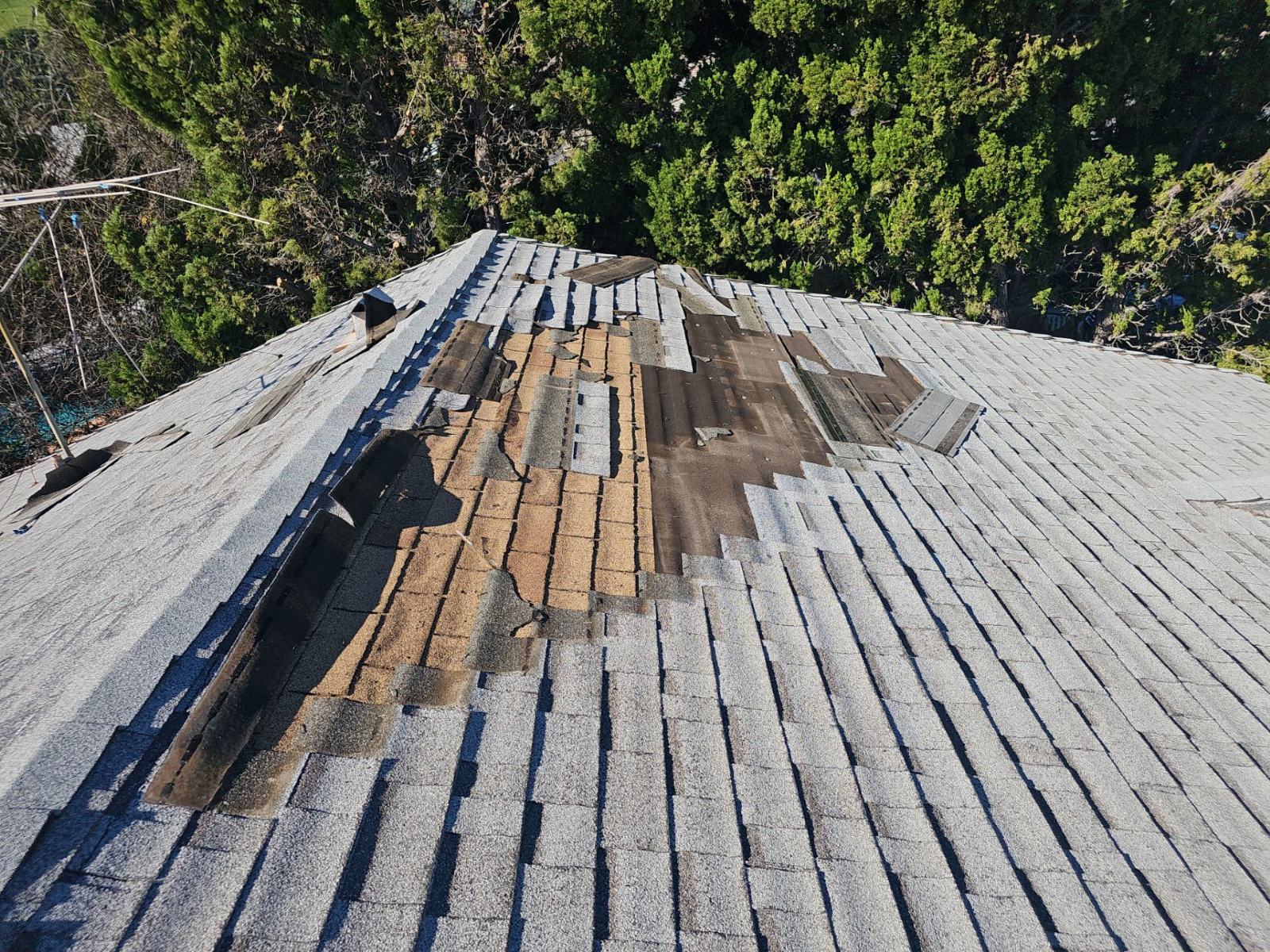 Severely damaged asphalt shingle roof with missing shingles exposing underlayment and decking — Roof Replacement Inc