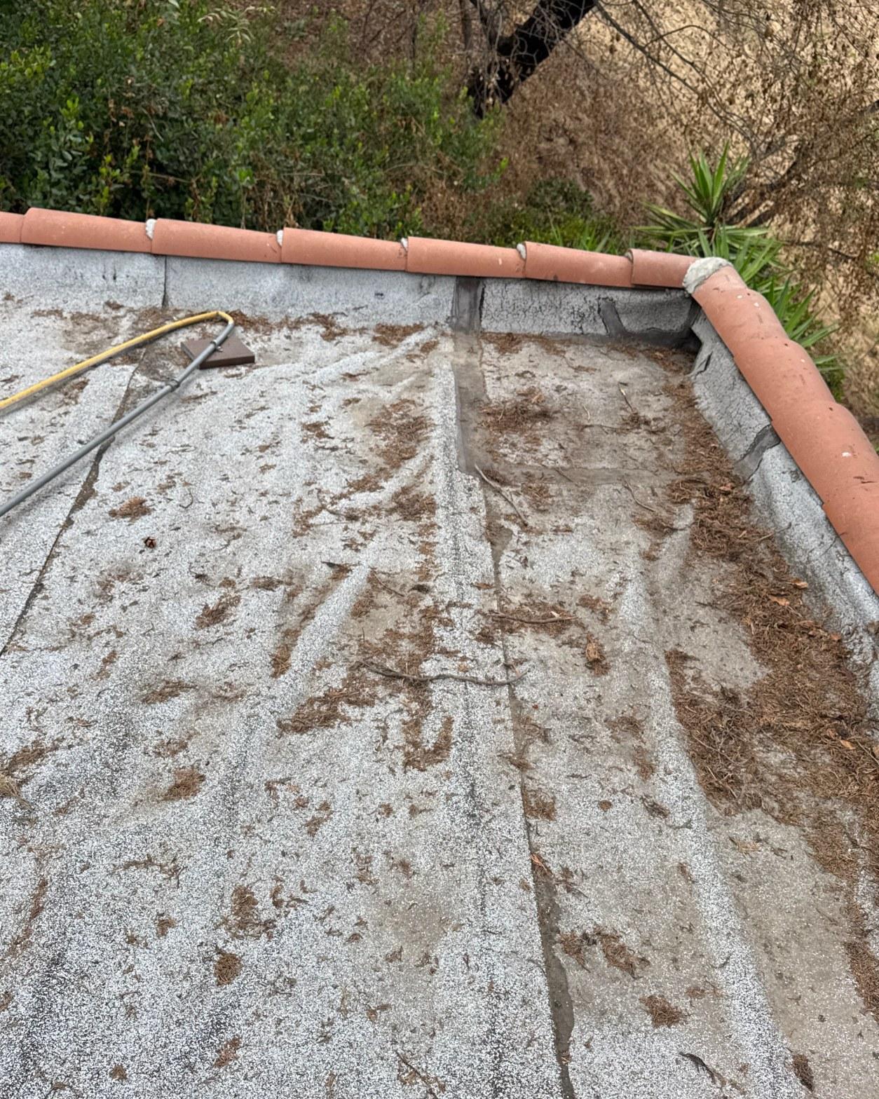 Debris-covered torch down flat roof with terracotta tile coping before tearoff in Los Angeles County