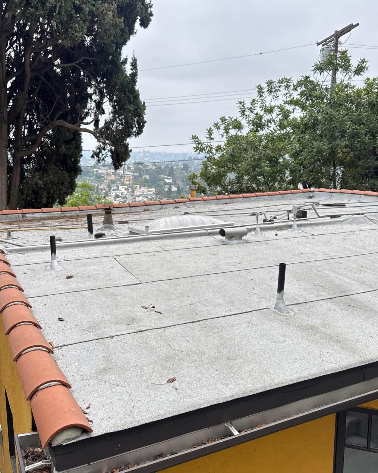 torch-down-flat-roof-replacement-insulation-los-angeles-3339 White gravel flat roof with black pipe vents, dome skylight, and terracotta tile edge trim on hillside home.