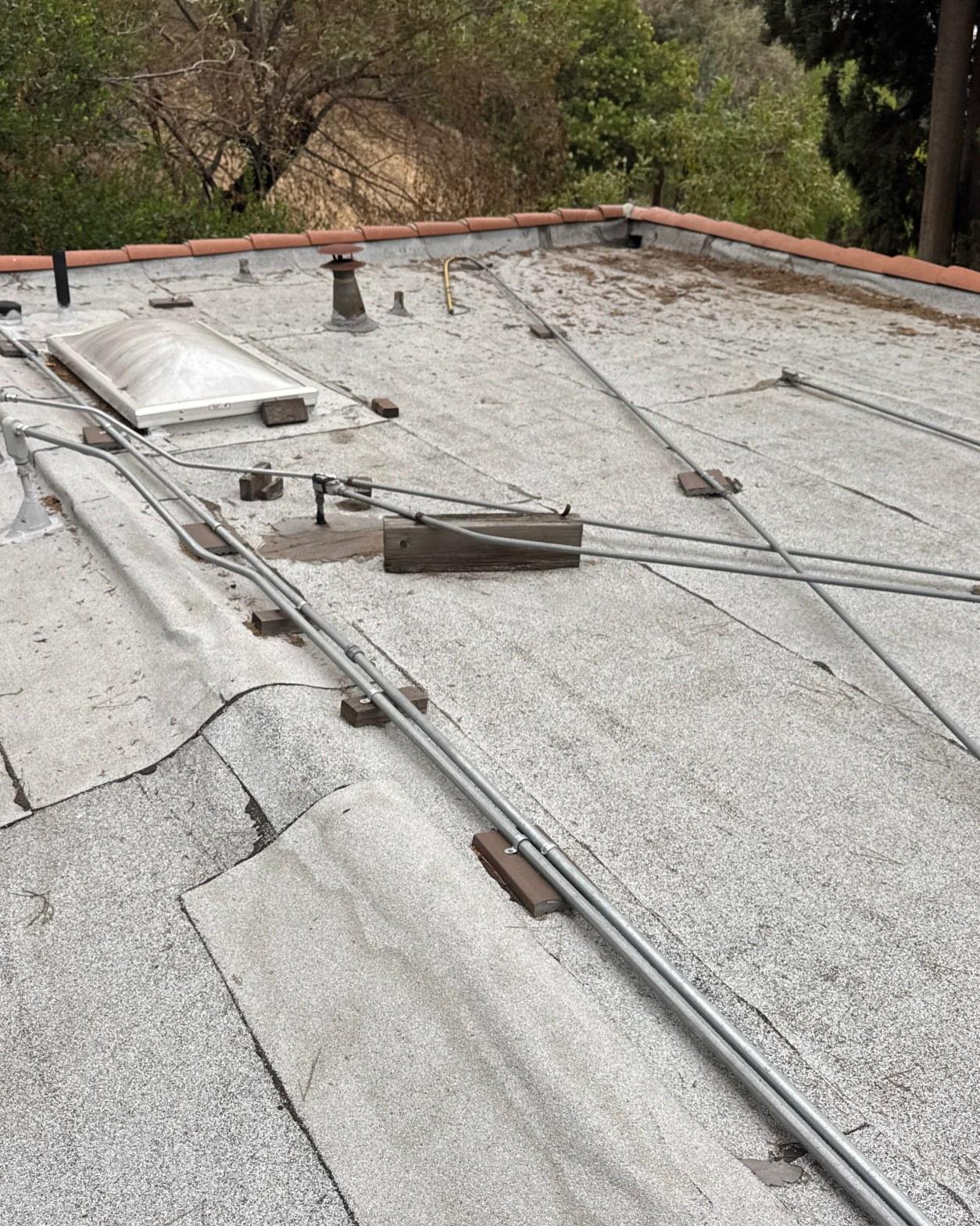 torch-down-flat-roof-replacement-insulation-los-angeles-3340 Weathered flat roof with electrical conduit lines, wood blocks, skylight, and vent pipe on residential building.