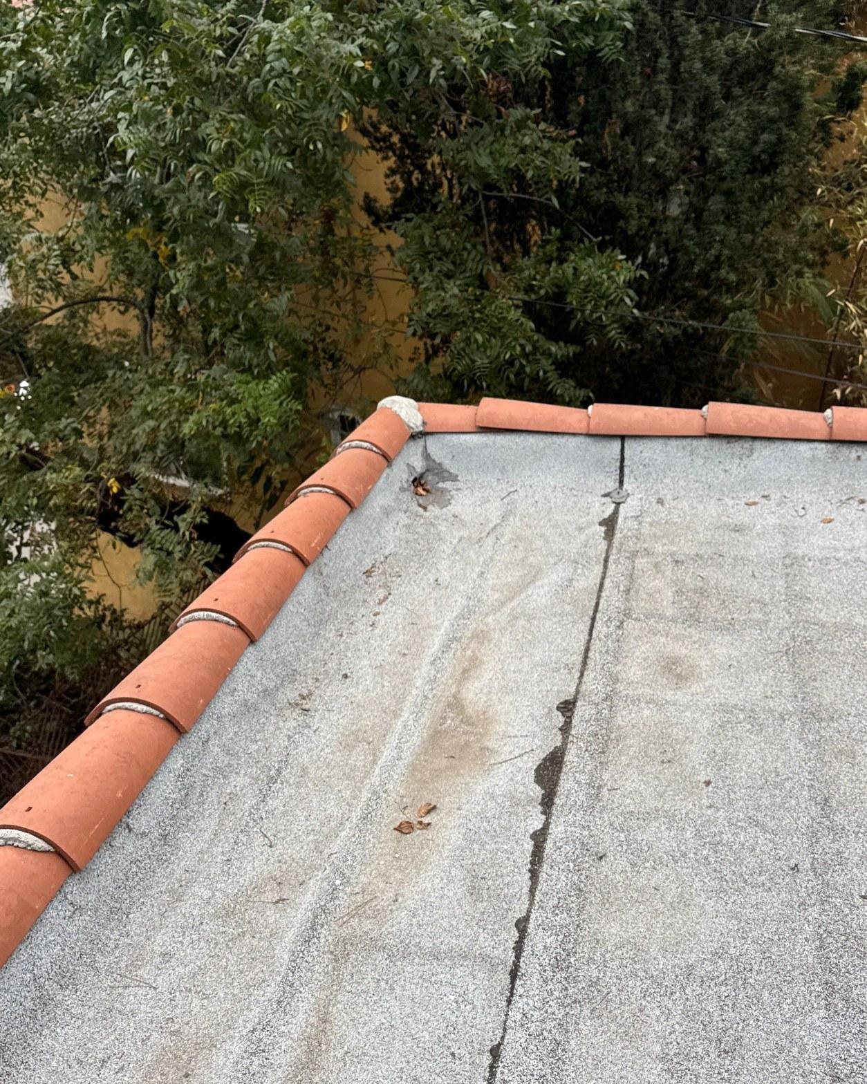 torch-down-flat-roof-replacement-insulation-los-angeles-3341 Cracked flat concrete roof surface with clay terracotta ridge tiles along the edge, showing water damage stains.
