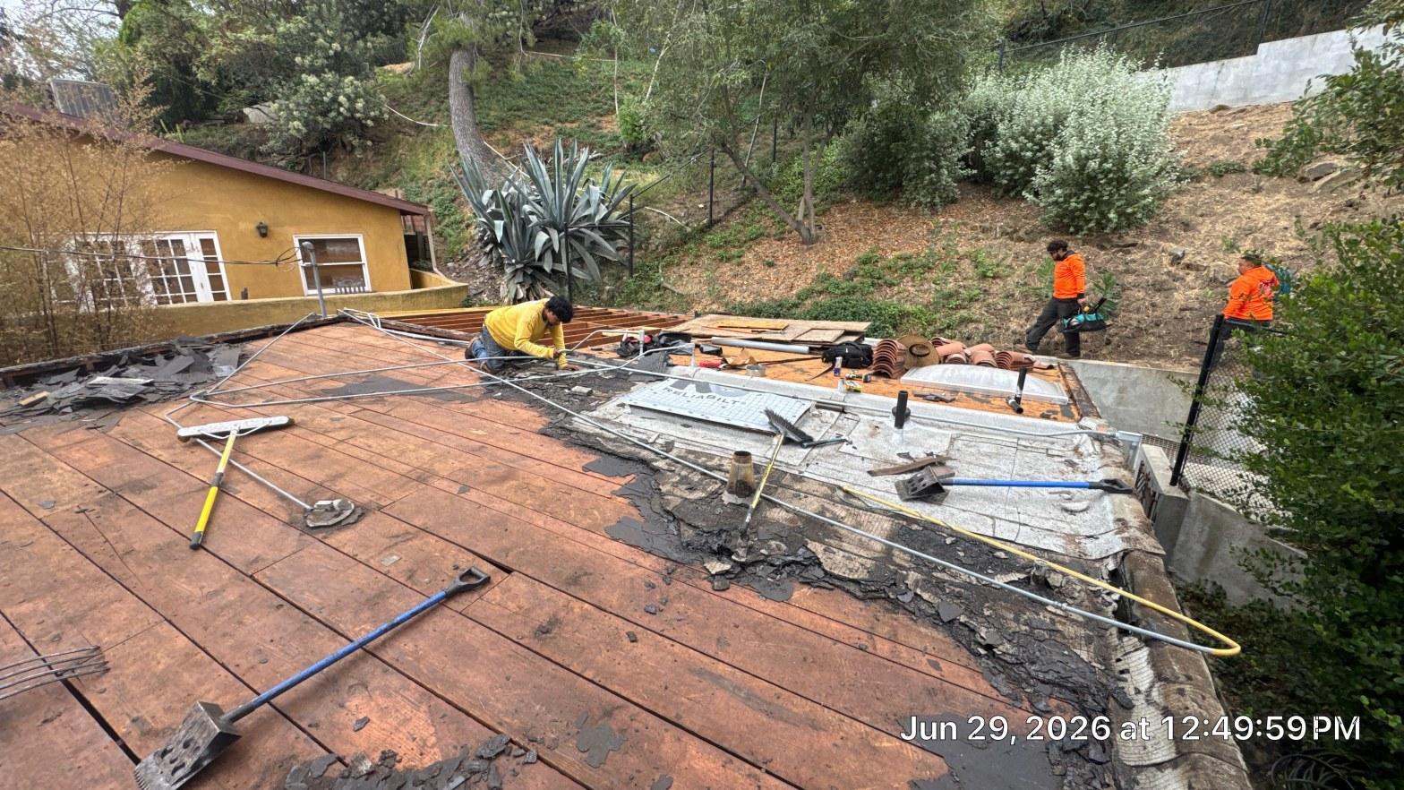 torch-down-flat-roof-replacement-insulation-los-angeles-3344 Three roofers removing old flat roof membrane and tiles, exposing wood decking on residential home, June 2026.