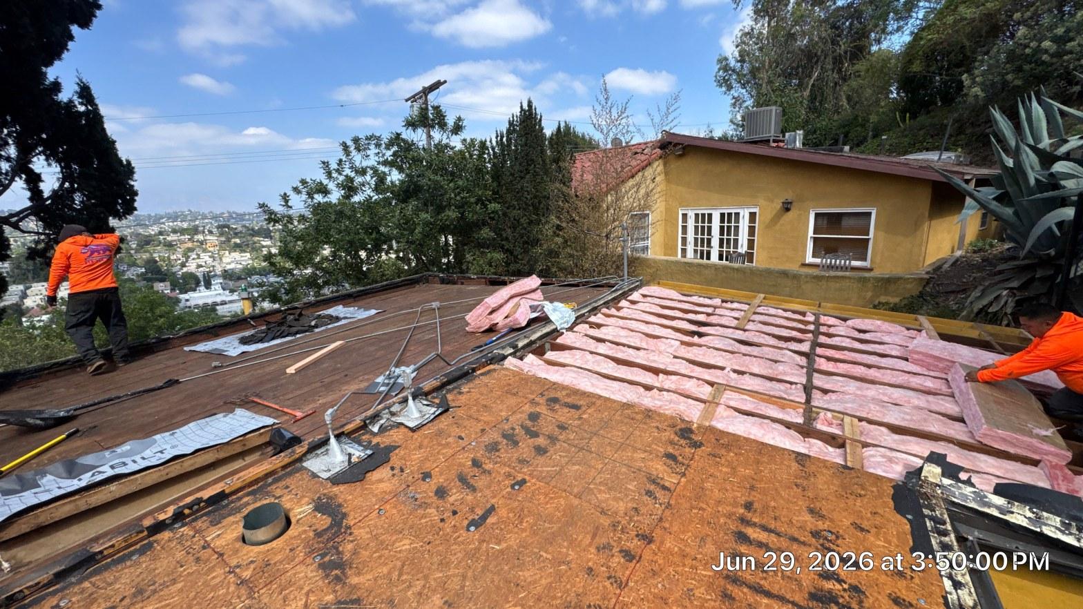 torch-down-flat-roof-replacement-insulation-los-angeles-3347 Roofing crew tearing off flat roof on hillside home, exposing OSB decking and pink fiberglass insulation batts.