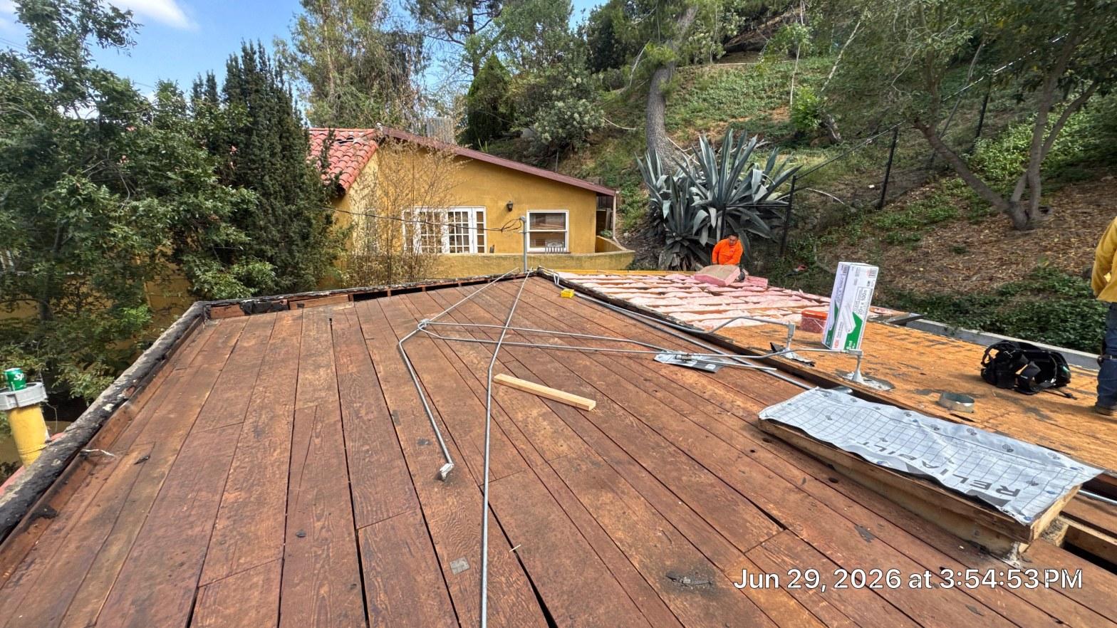 torch-down-flat-roof-replacement-insulation-los-angeles-3348 Exposed wood roof decking during tear-off with worker laying underlayment on residential home in wooded hillside.