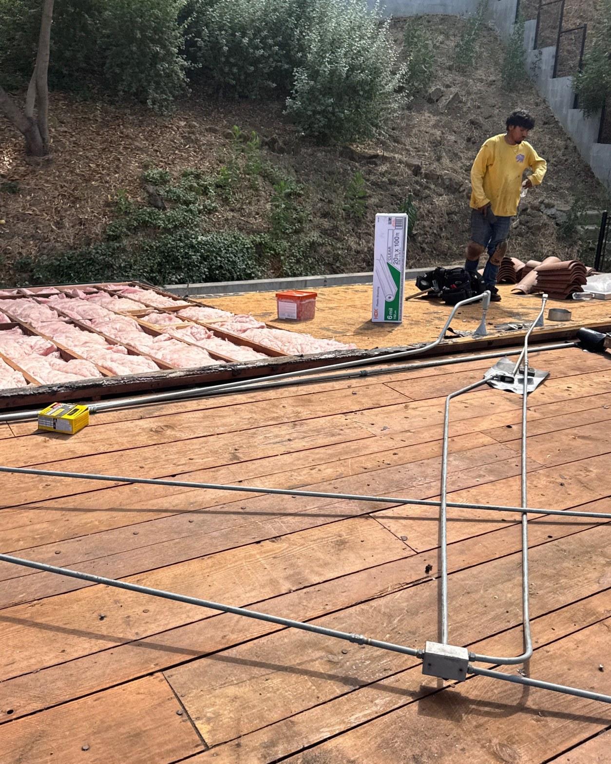 torch-down-flat-roof-replacement-insulation-los-angeles-3350 Roofing contractor in yellow shirt on bare wood roof deck with fiberglass batt insulation and conduit exposed.