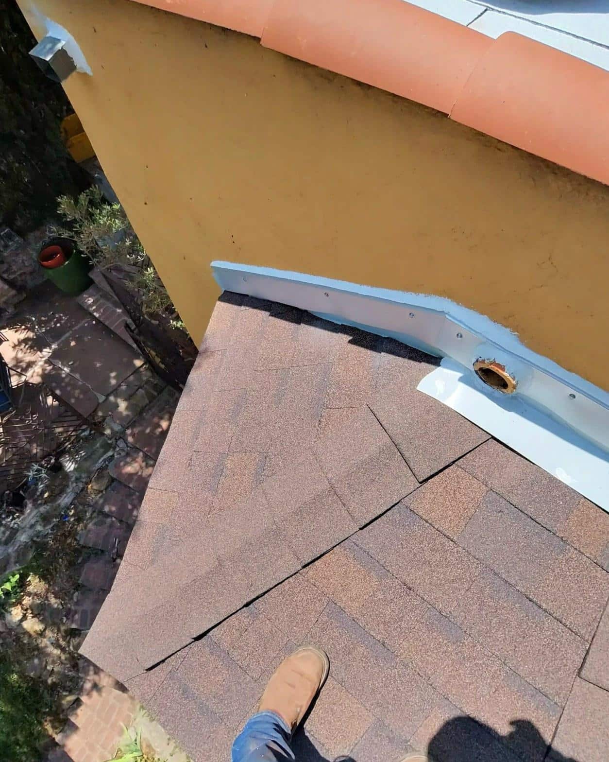 torch-down-flat-roof-replacement-insulation-los-angeles-3359 Close-up of asphalt shingle roof meeting yellow stucco parapet wall with white metal flashing and open pipe penetration.