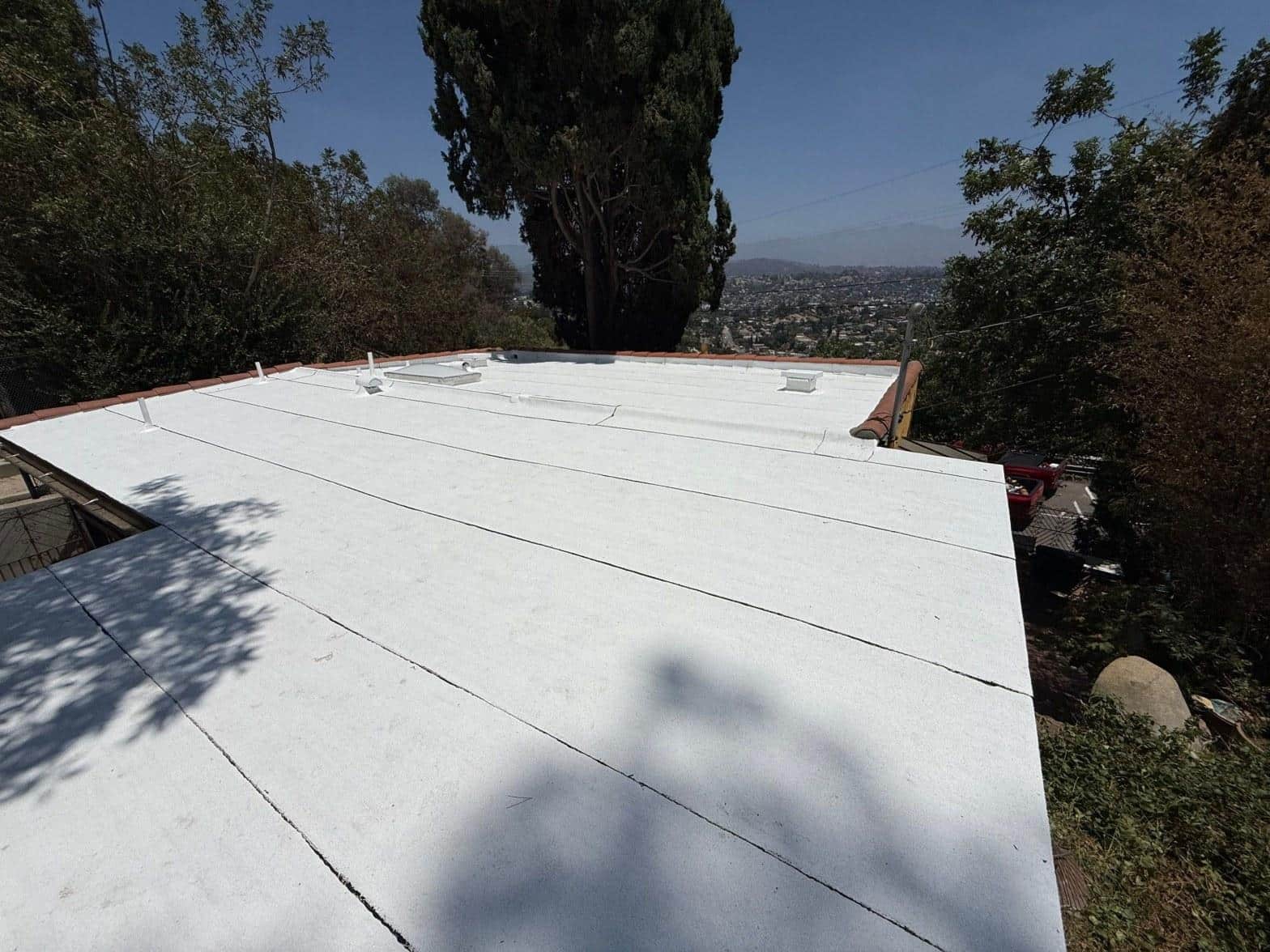 torch-down-flat-roof-replacement-insulation-los-angeles-3360 Newly installed white TPO flat roof membrane with skylights on hillside home, Los Angeles city view in background.
