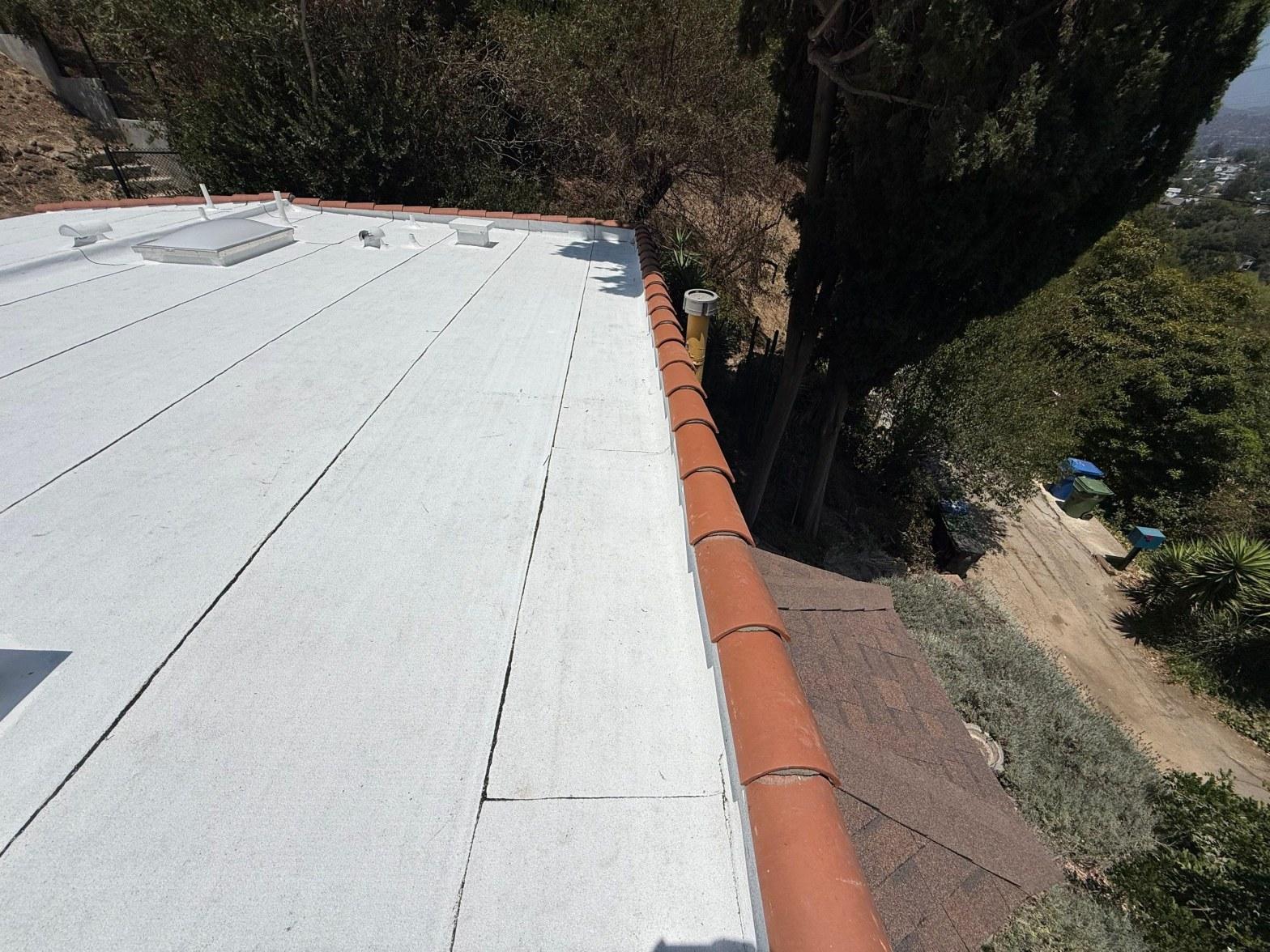 torch-down-flat-roof-replacement-insulation-los-angeles-3363 White foam flat roof with red clay tile edge cap, skylights, and asphalt shingle lower section on hillside home.
