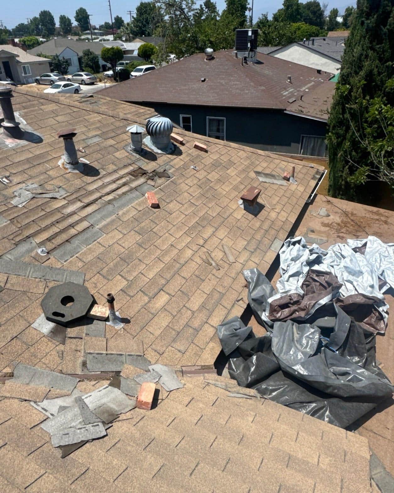 Mid-inspection view of severely deteriorated composition shingles with failed pipe boots and turbine vents on an LA County home