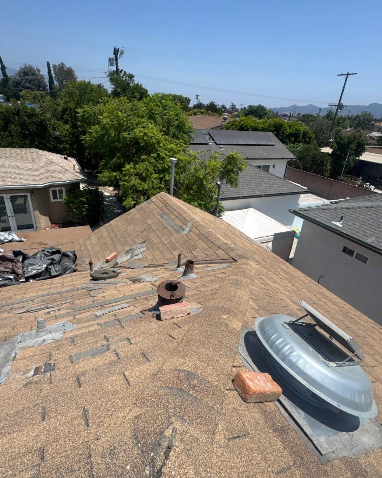 Shingle tear-off in progress showing stripped penetrations, corroded boot flashings, and debris collected on the roof slope