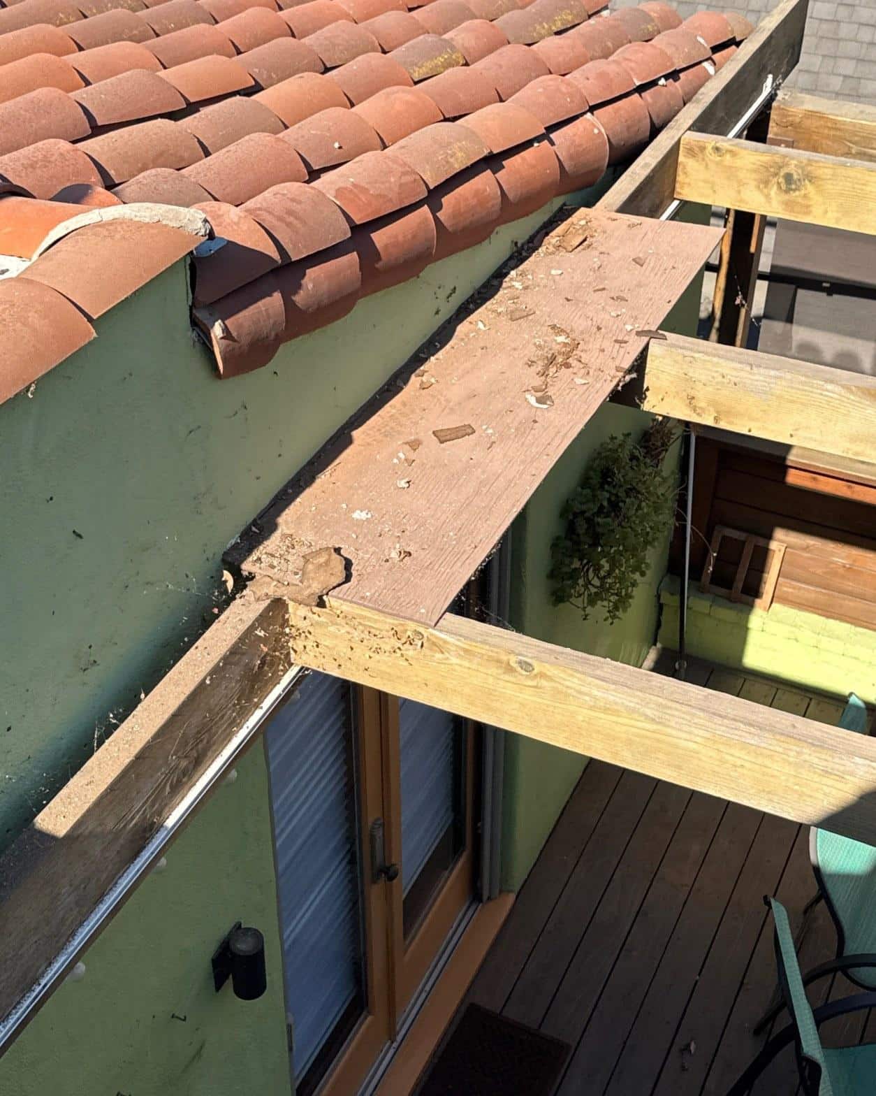 Rotted wood fascia board with tile debris beside clay tile roof during replacement project