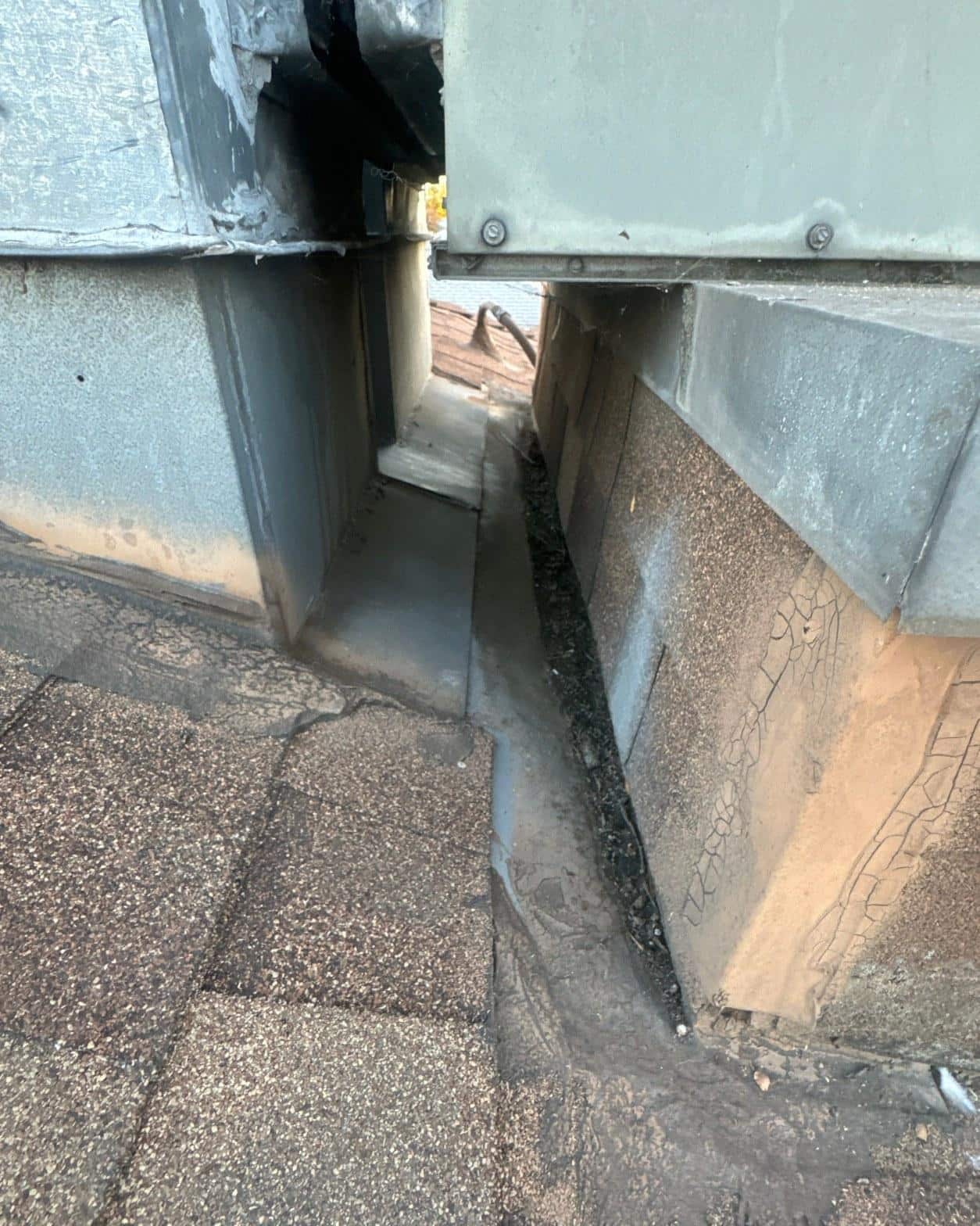 Open HVAC curb flashing joint showing gap between sheet metal curb pan and shingle field on residential roof