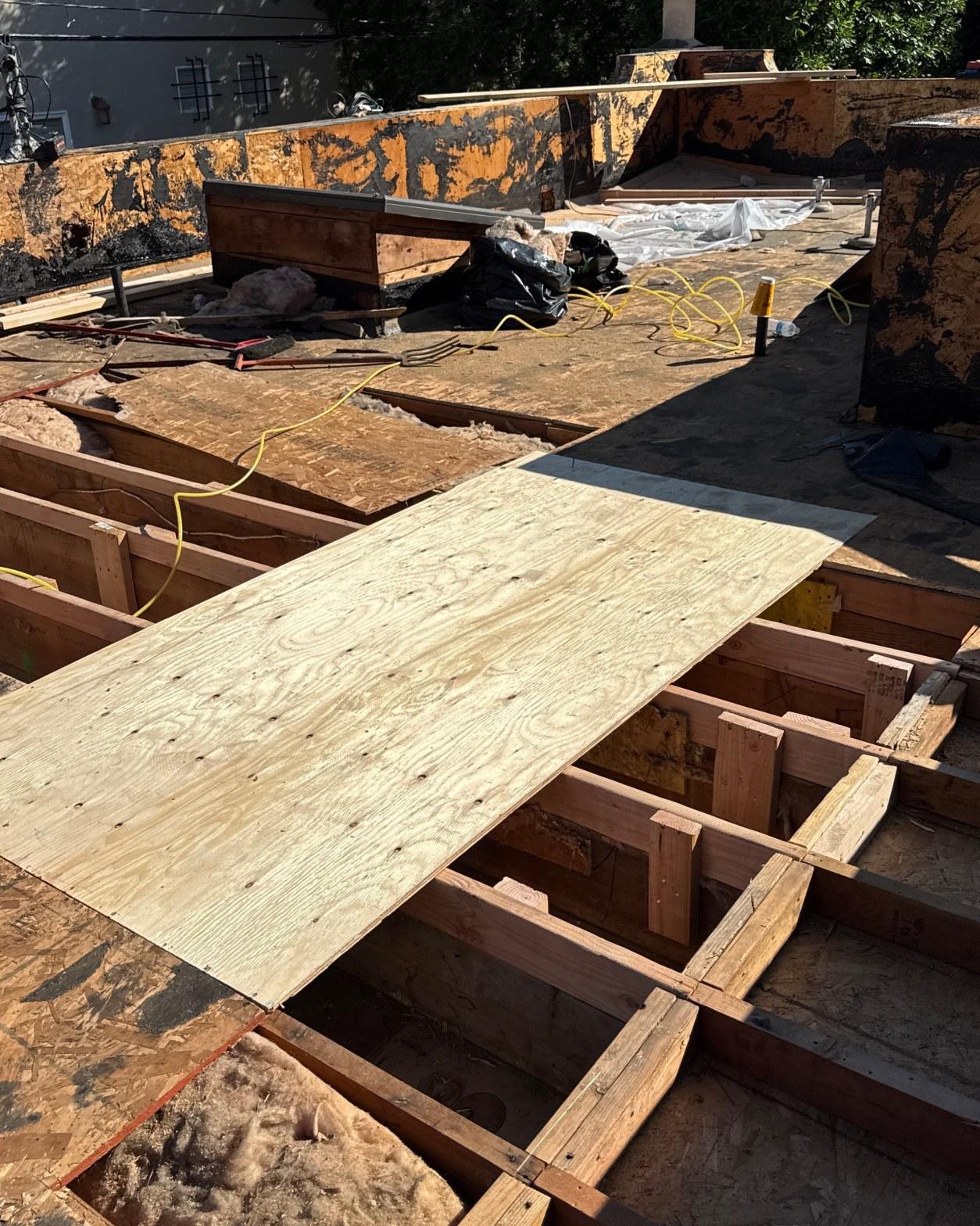 Mid-rebuild flat roof showing new OSB sheathing panels beside deteriorated framing and old bituminous decking material