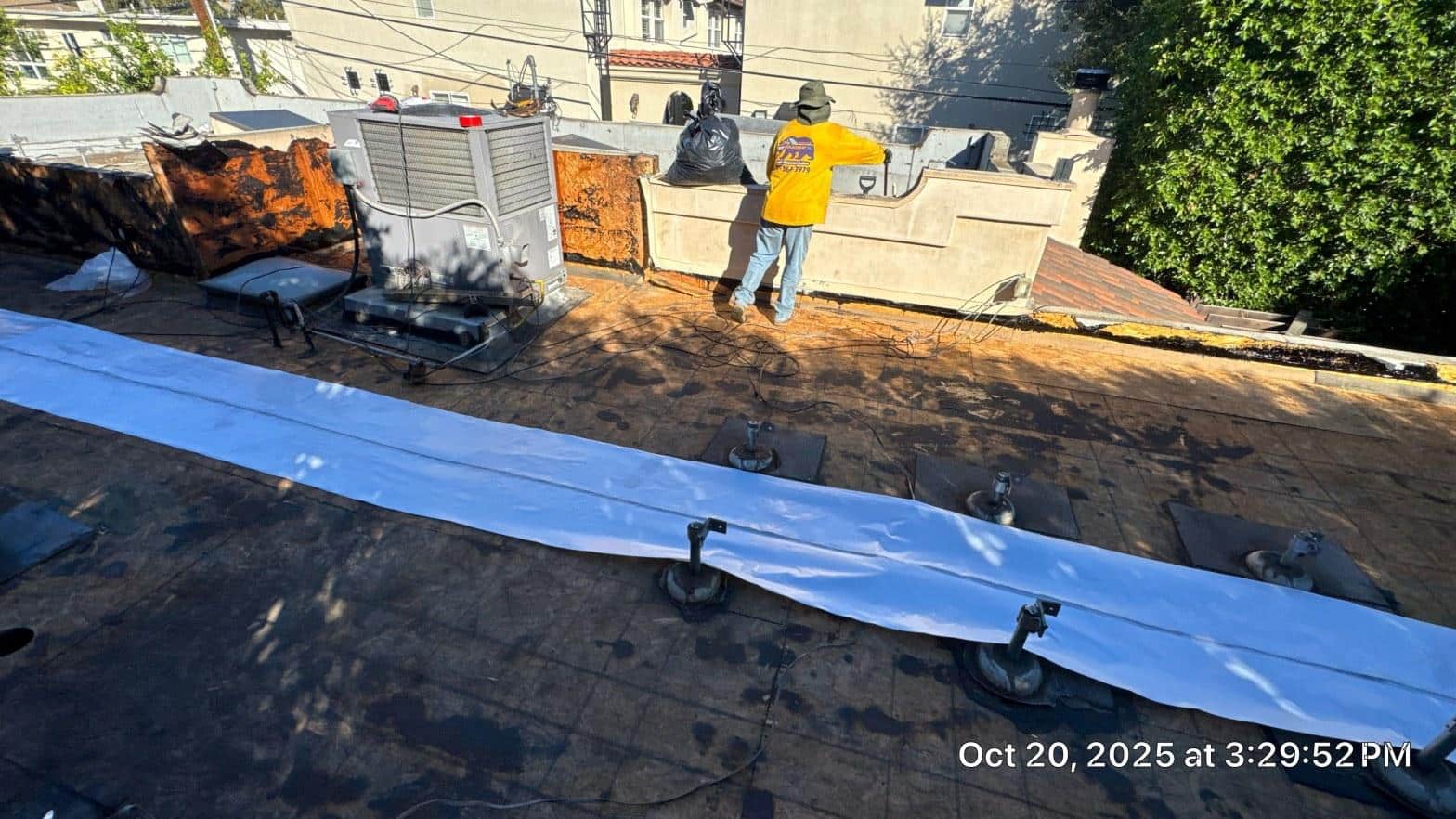 Crew member unrolling white reflective low-slope membrane across rebuilt flat roof deck with HVAC equipment and parapet visible