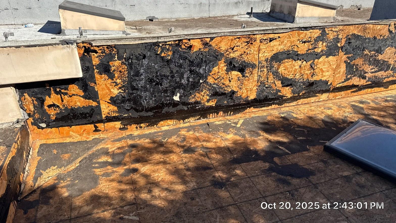 Stripped parapet sheathing showing old bituminous mastic and fresh OSB before new membrane was lapped and sealed to the wall