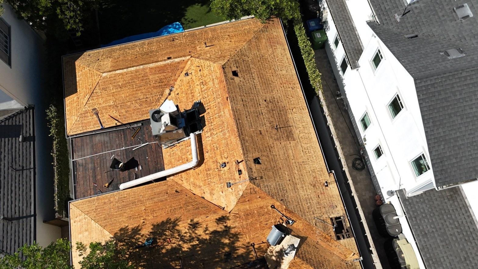 Aerial drone view of fully stripped plywood decking across a multi-hip residential roof mid-reroof project