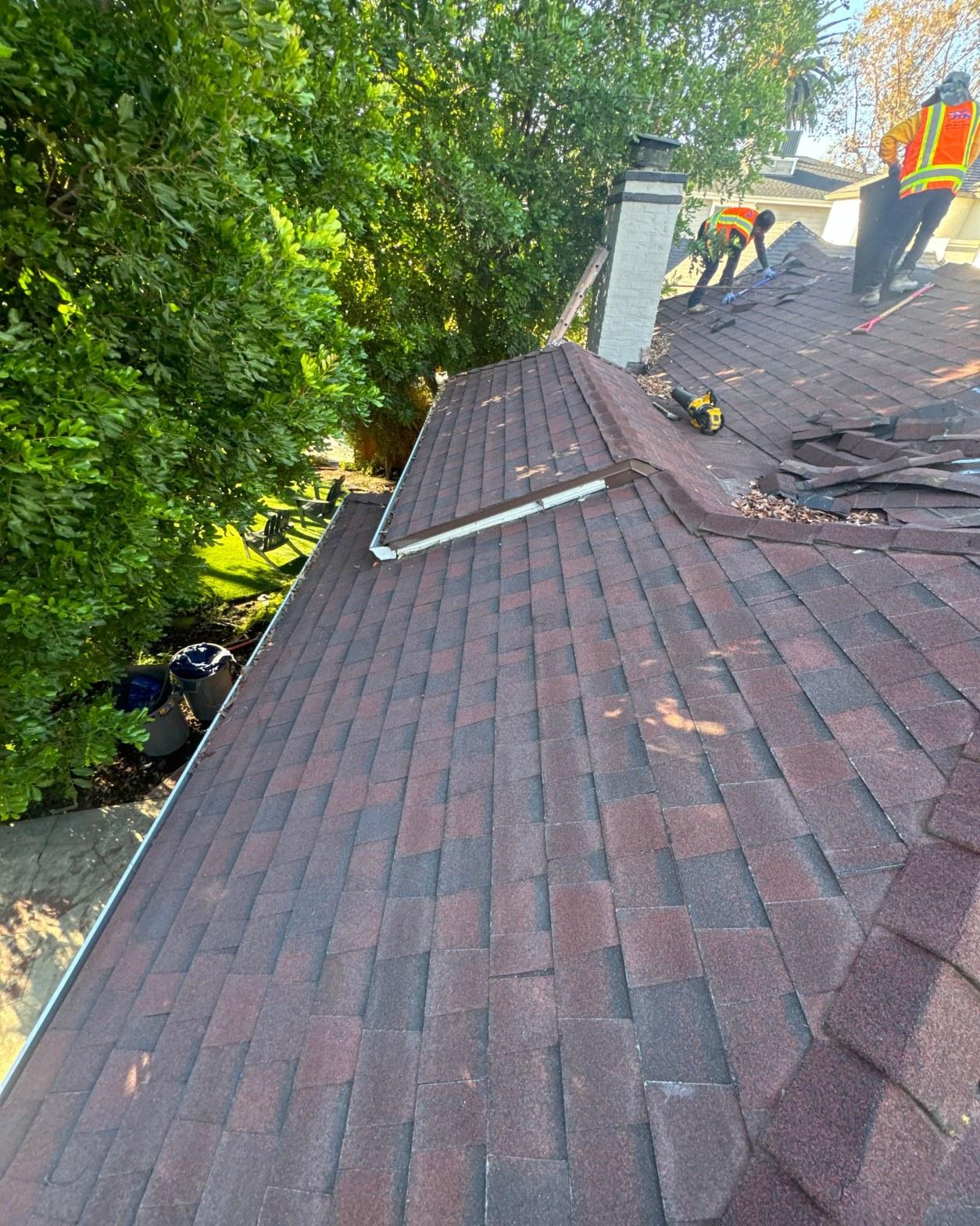 New dark charcoal composition shingles installed on a section of the finished reroof with crew working in background