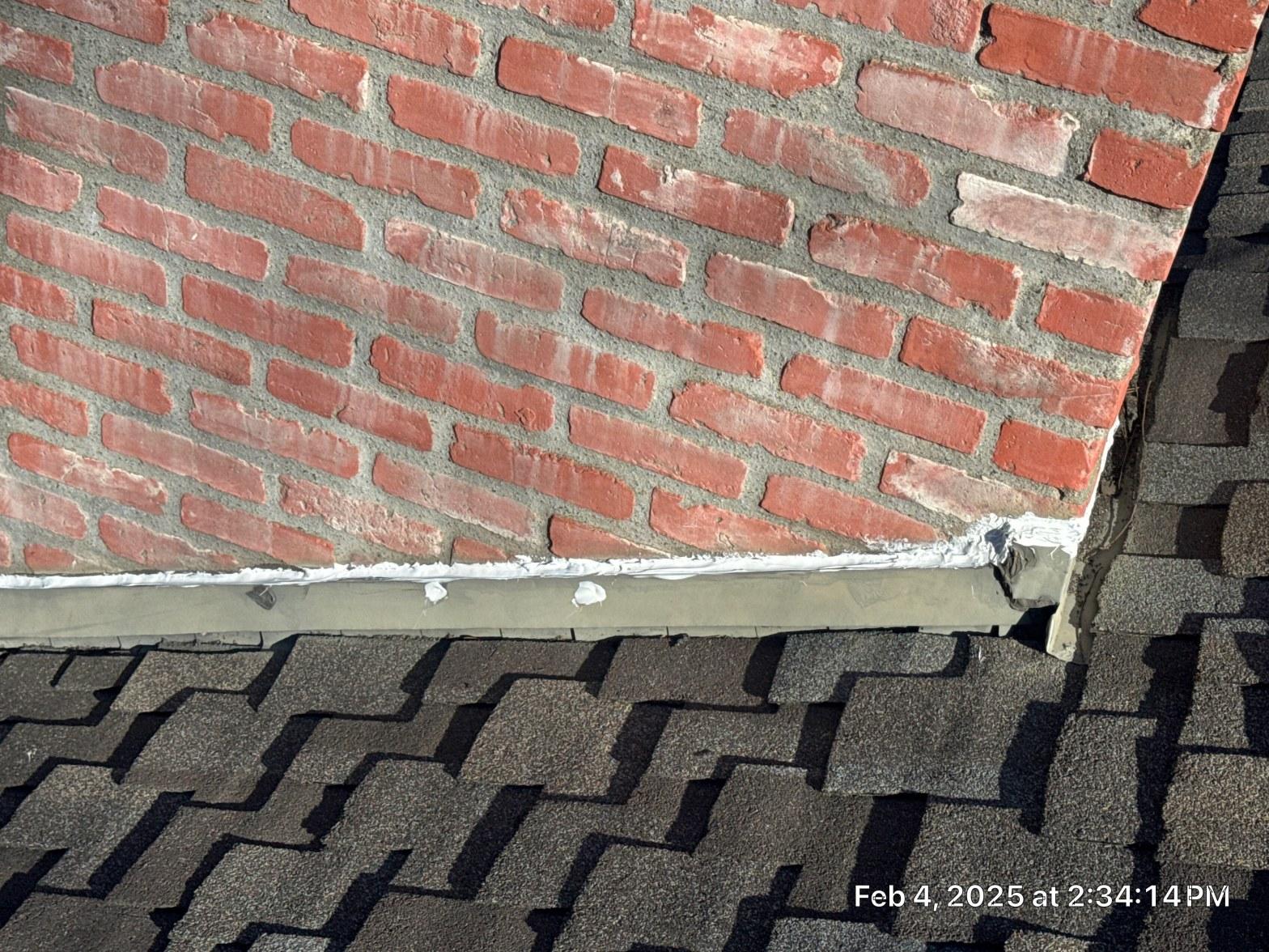 Deteriorated caulk bead on brick chimney apron flashing showing split gap above asphalt shingles