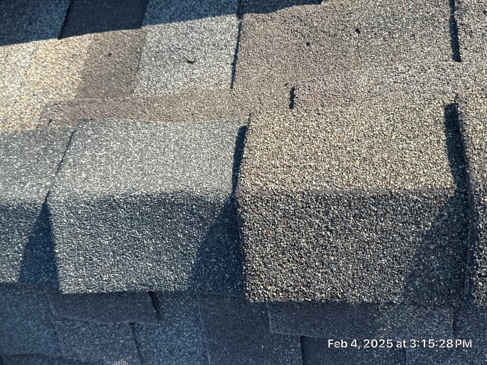 Granule-depleted asphalt shingles showing exposed mat and surface cracking on residential roof field