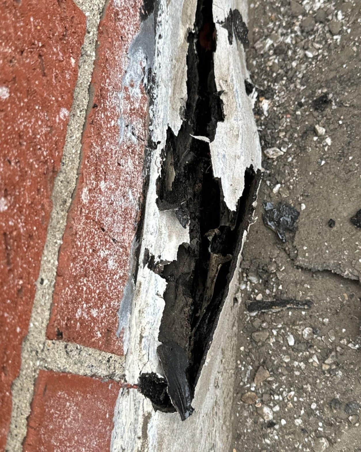 Failed chimney flashing on a low-slope roof showing delaminated bitumen and separated layers at brick parapet