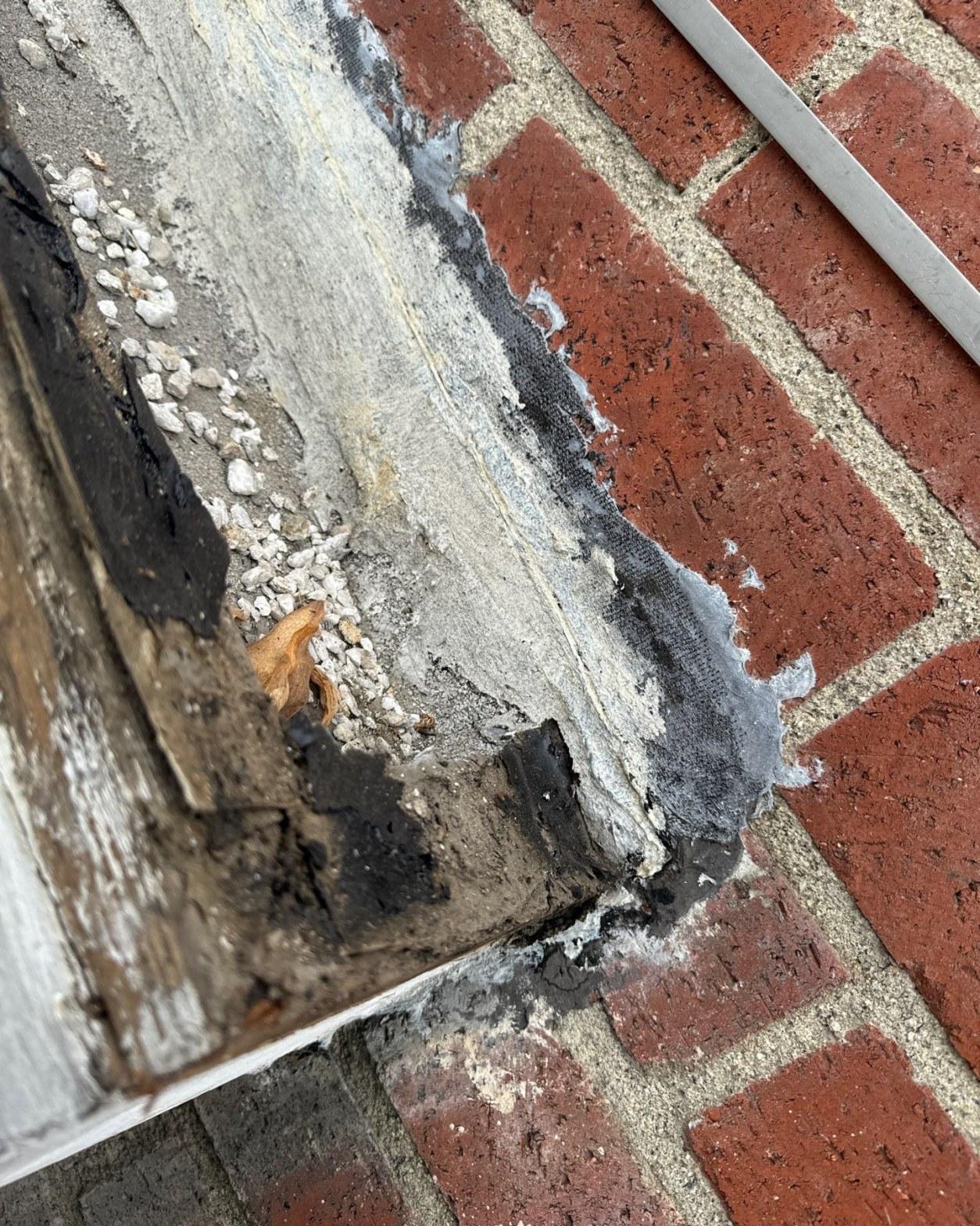 Deteriorated parapet corner flashing at brick chimney with exposed substrate and loose gravel before rebuild
