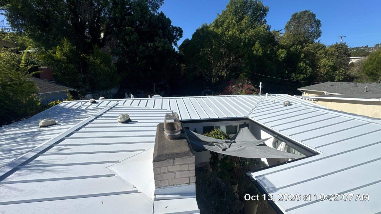 Completed standing-seam metal roof panels running past the brick chimney on the mid-century courtyard home
