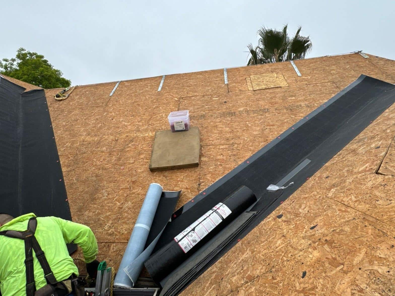 Roofer staging underlayment rolls on fresh OSB decking during a multi-unit shingle reroof in the San Fernando Valley