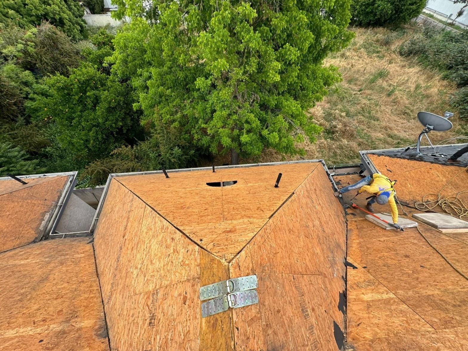Roofer fastening new OSB sheathing panels on intersecting hip roof planes during a full deck replacement project