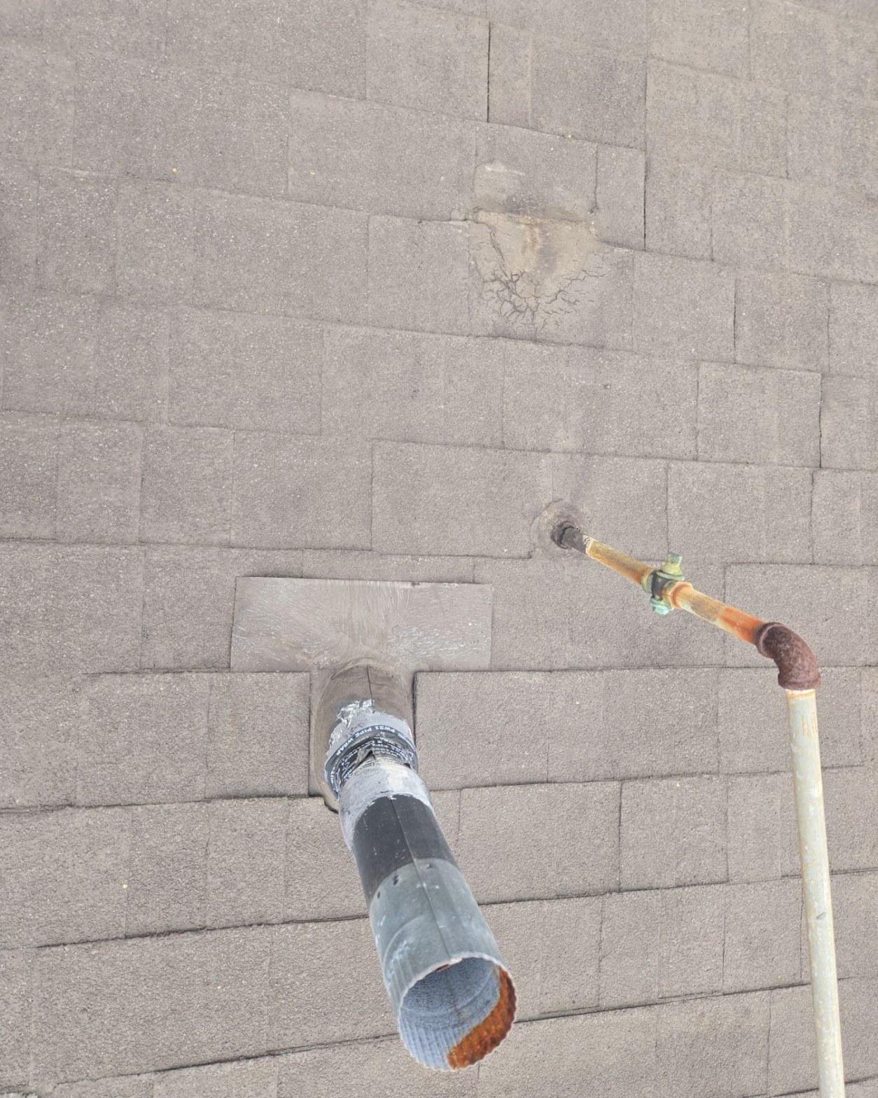 New vent boot flashing set into fresh shingles with a corroded copper pipe penetration visible nearby on an asphalt shingle roof