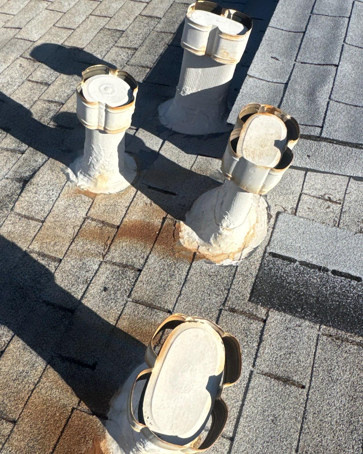 Close-up of old ceramic pipe caps with failed spray-foam bases on a worn asphalt shingle roof before reset