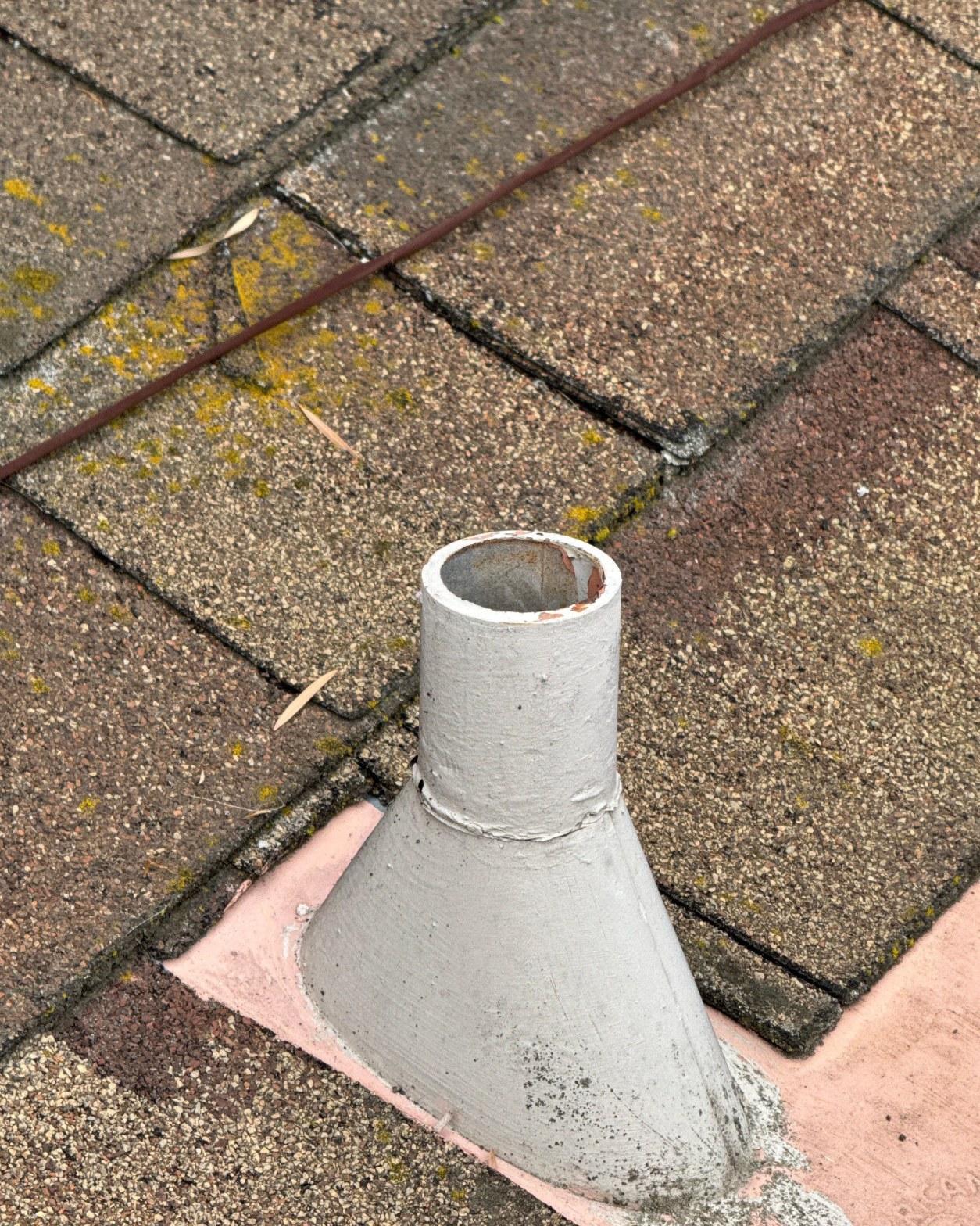 Cracked lead plumbing vent jack with failed caulk seal on worn shingle roof before replacement