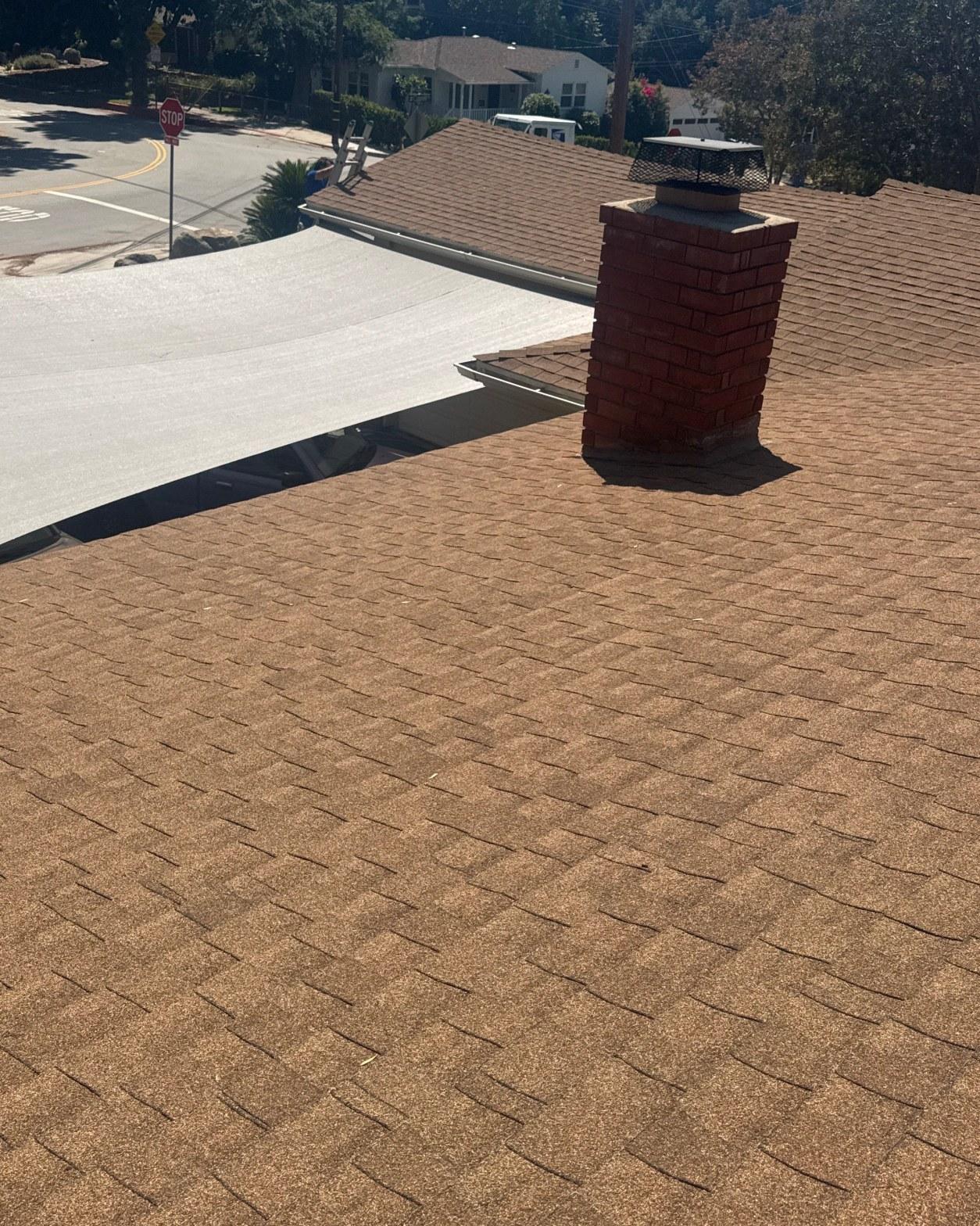 shingle-reroof-monrovia-3392 Newly installed brown asphalt shingle roof with red brick chimney and flat roof section, residential neighborhood.