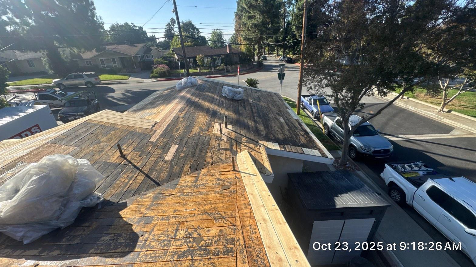 shingle-reroof-monrovia-3401 Stripped roof deck with exposed wood planks and bundled debris on residential building at street corner.