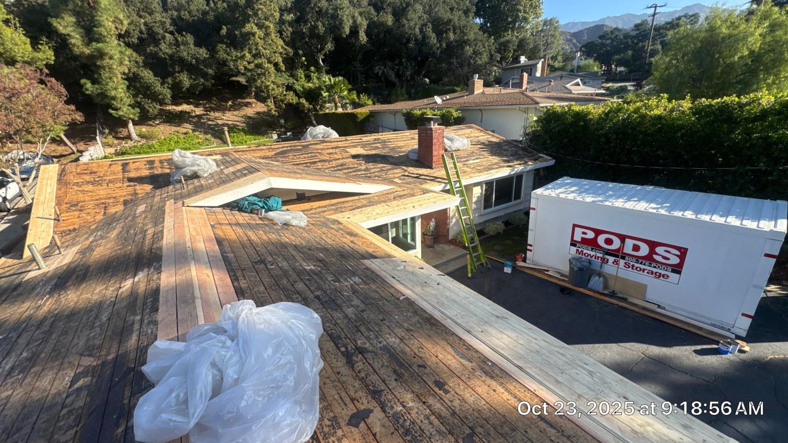 shingle-reroof-monrovia-3402 Roof tear-off exposing plank wood decking on flat residential home with ladder, PODS storage container in driveway.